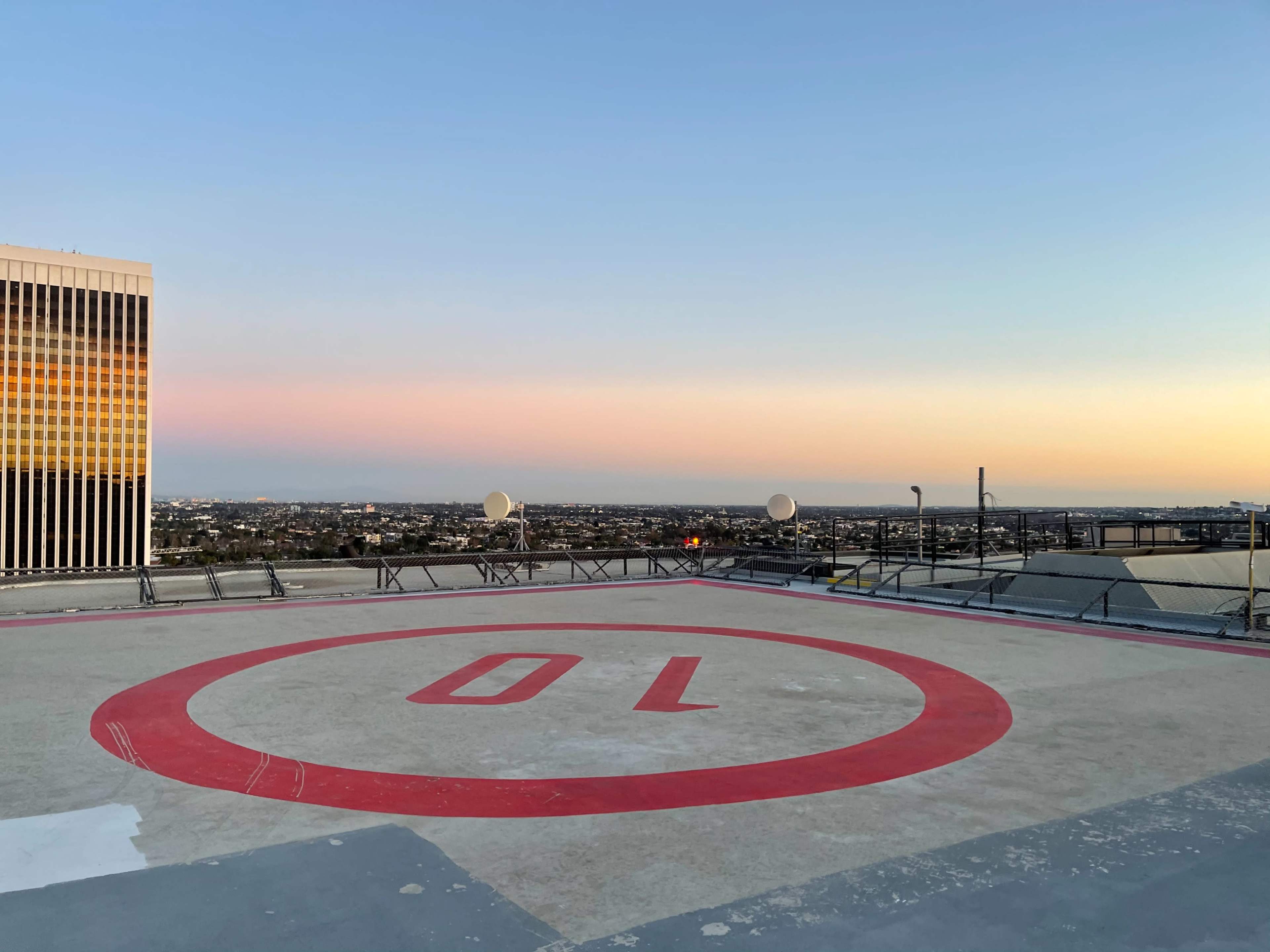 A rooftop helipad marked with the number 70 overlooks a city skyline during sunset.