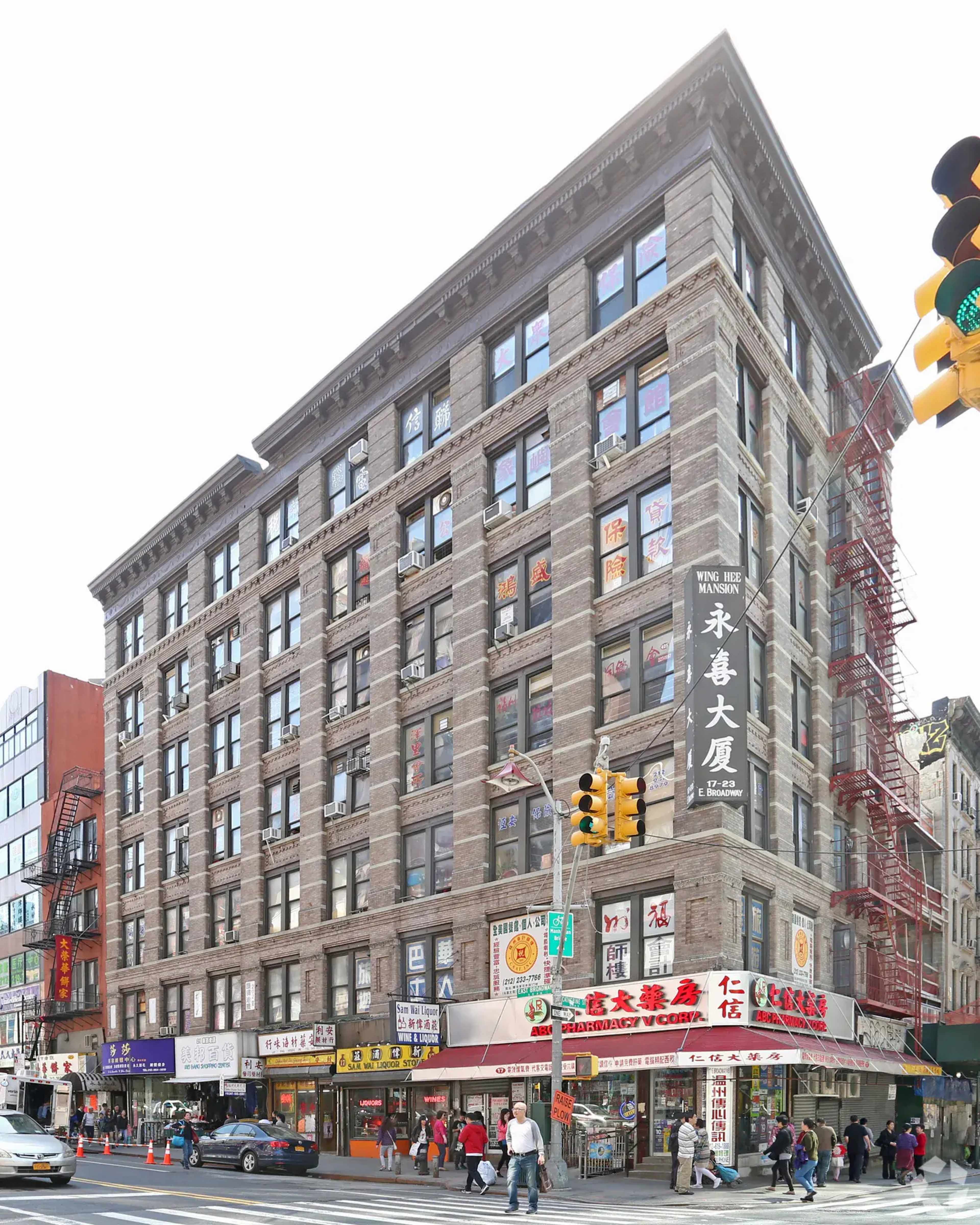 A multi-story brick building on a busy street, featuring ground-level shops and a prominent sign with Chinese characters.
