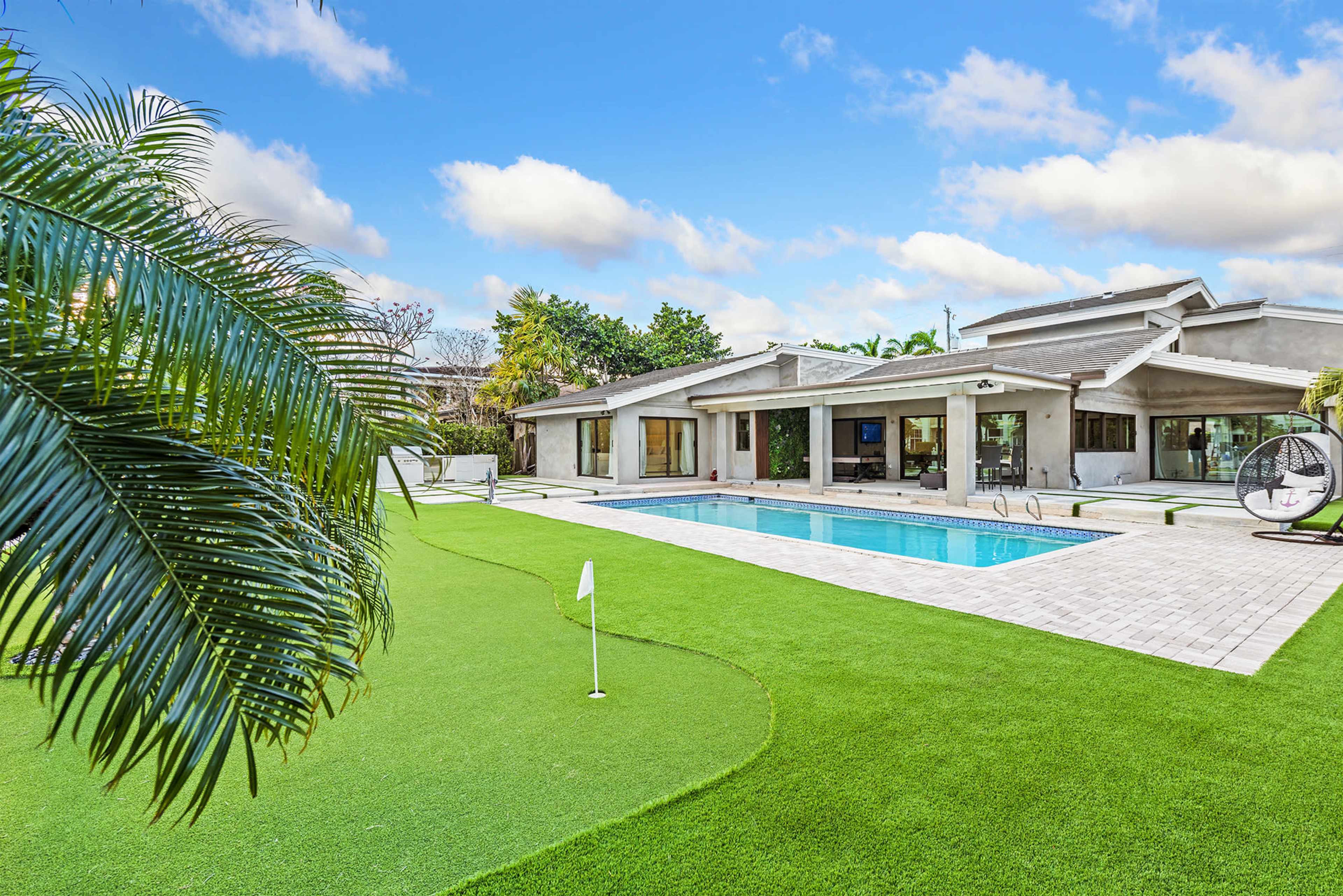 A modern house with a swimming pool and a well-maintained lawn featuring a putting green.