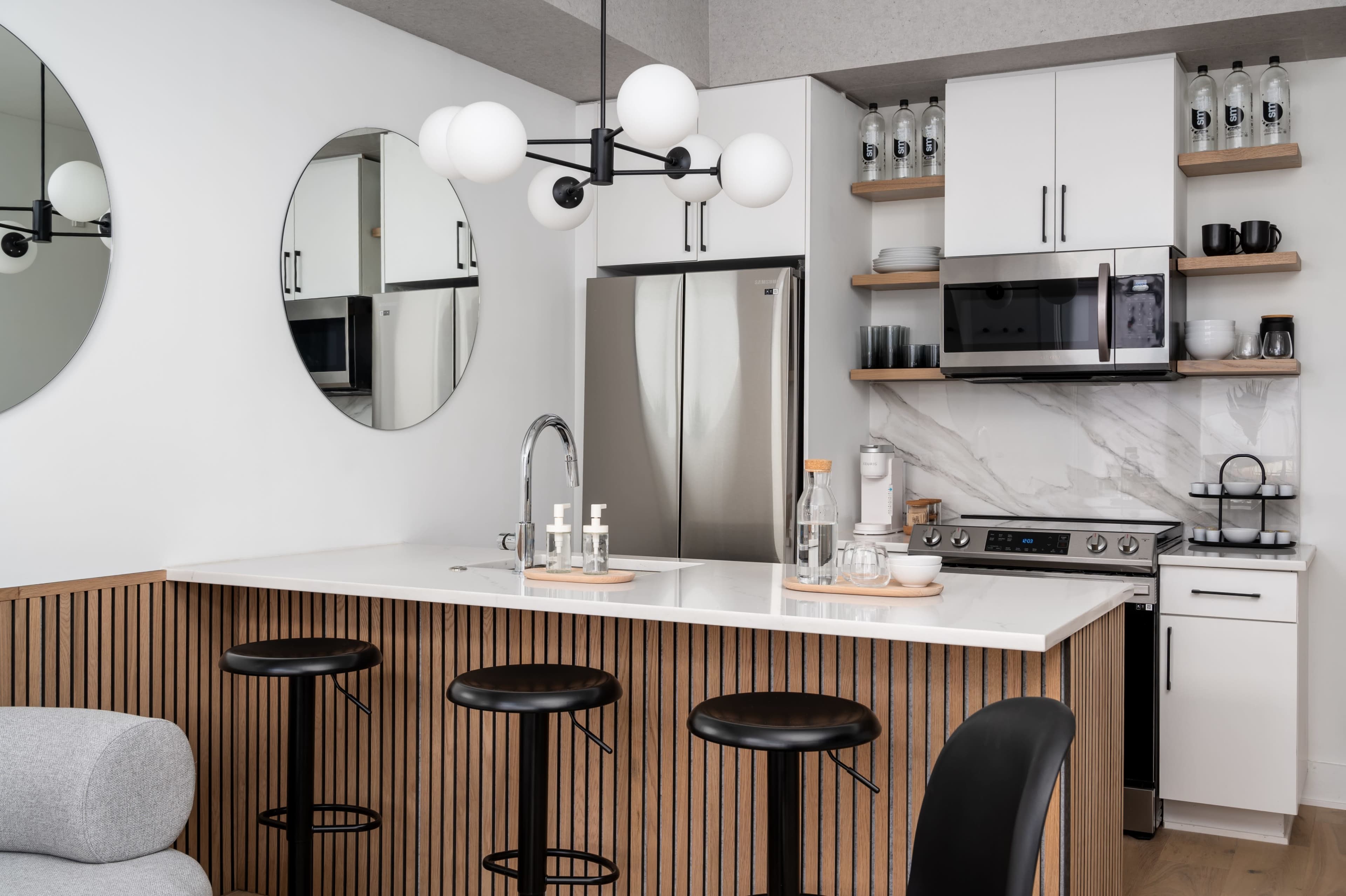 A modern kitchen with a central island, black bar stools, stainless steel appliances, and round mirrors on the wall.