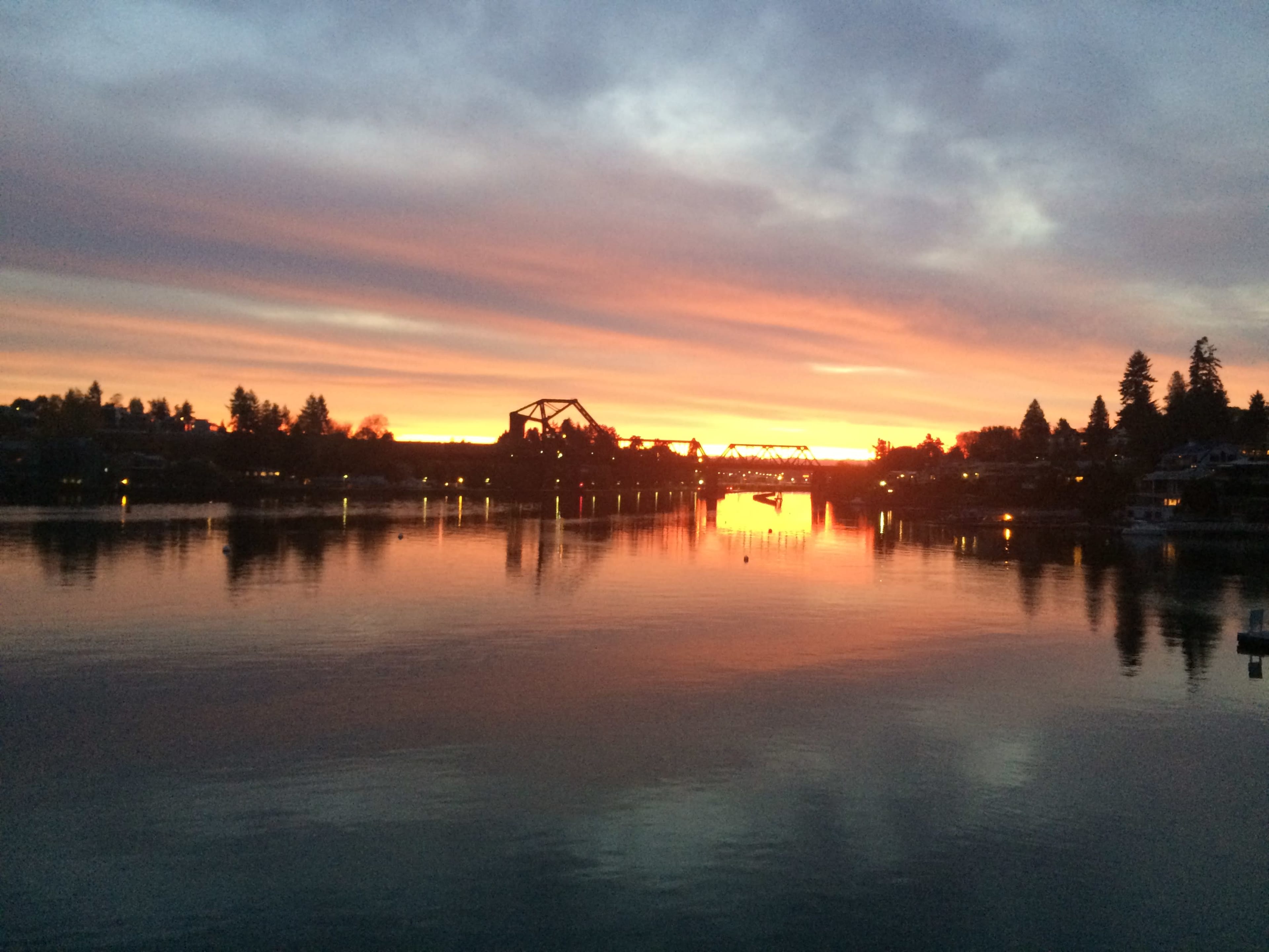 The image shows a river at sunset with a reflective surface and silhouettes of buildings and trees along the shore.