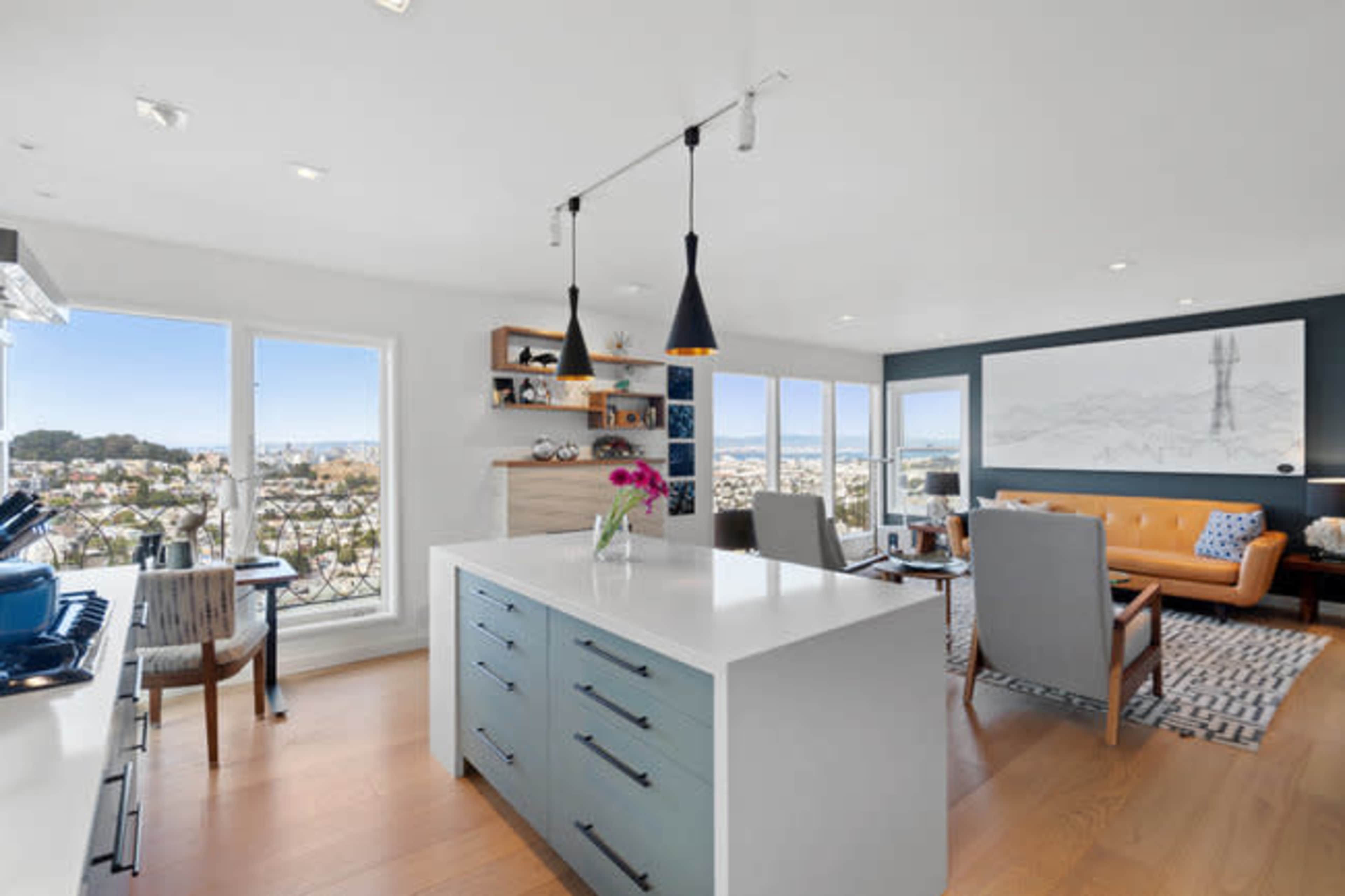 A modern kitchen and living area with a large island, stylish seating, and large windows showcasing a view of the city.