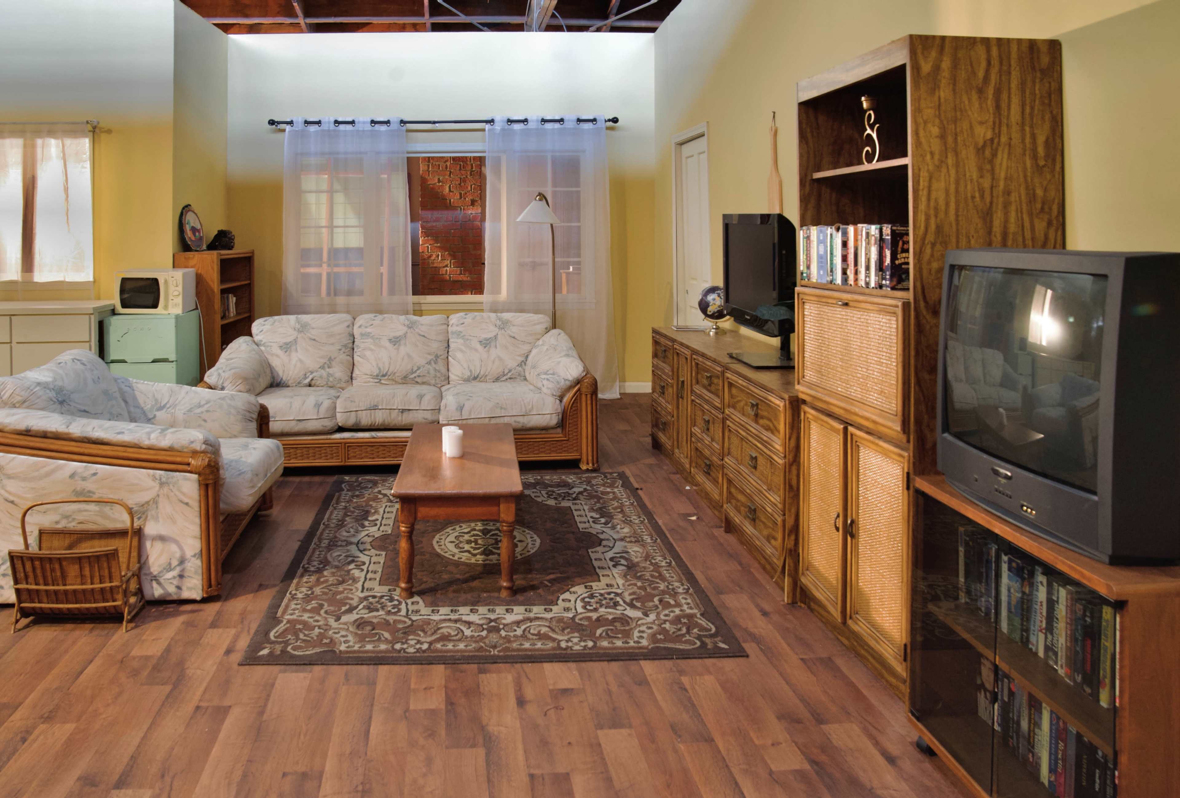 A living room features two light-colored sofas, a wooden coffee table, a patterned area rug, a television, and a cabinet against the wall.