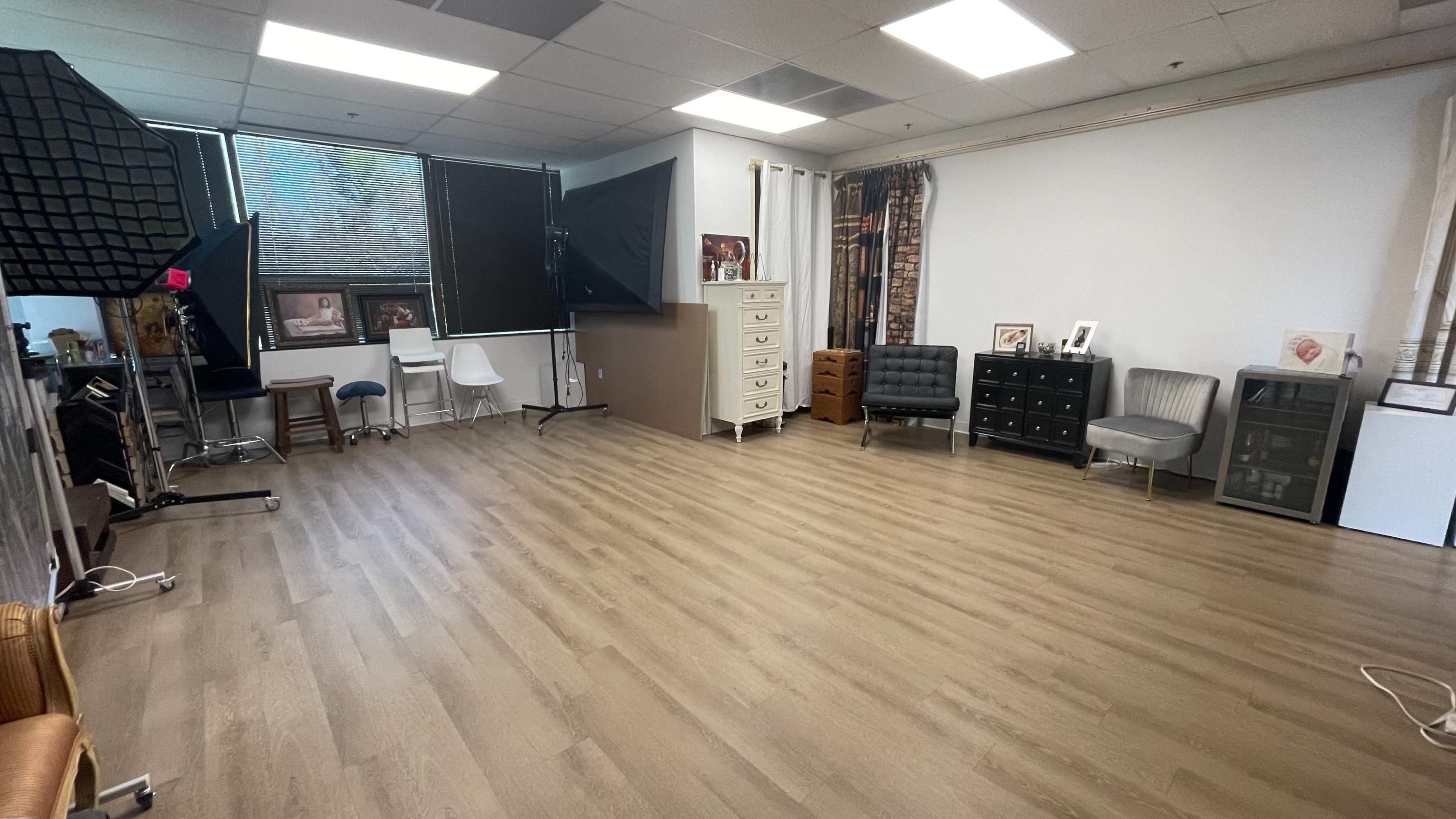 The image shows a spacious, well-lit studio with various pieces of furniture, including chairs and dressers, arranged around a wooden floor.