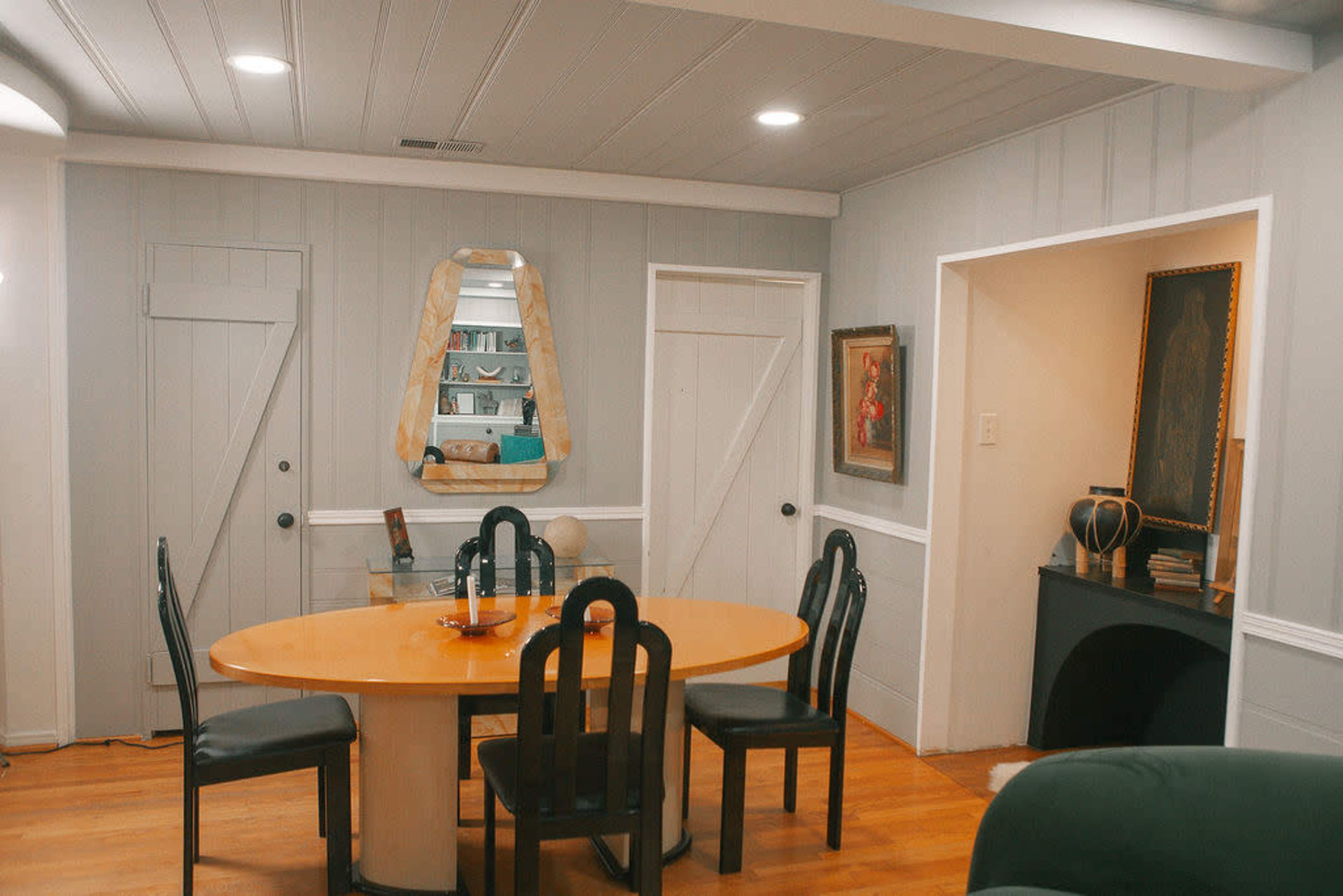 A dining area with a round table surrounded by black chairs, flanked by two doors and featuring a mirror on the wall.