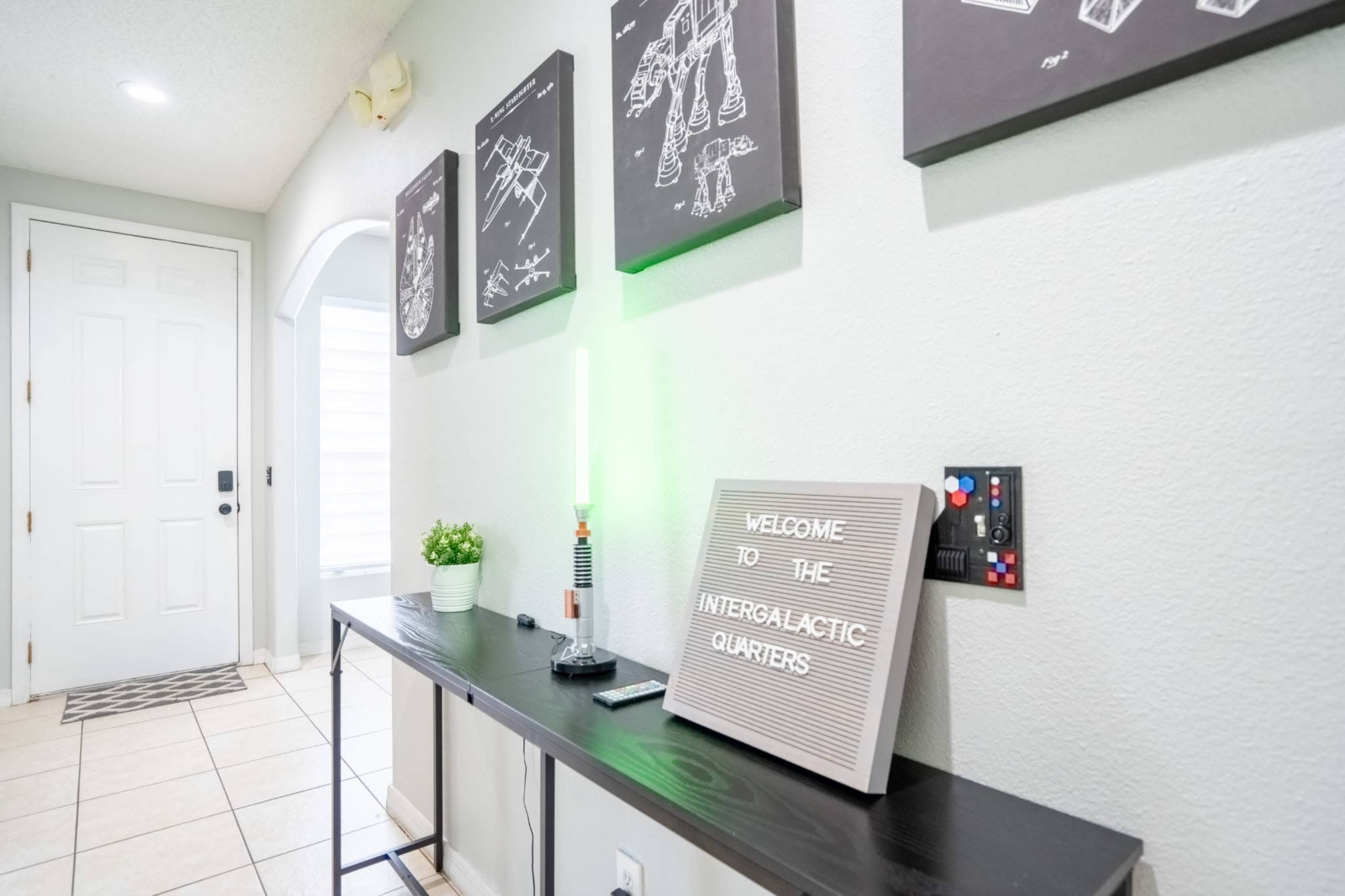 A modern entryway features a long black table with a light-up sign, decorative plant, and wall art displayed above.