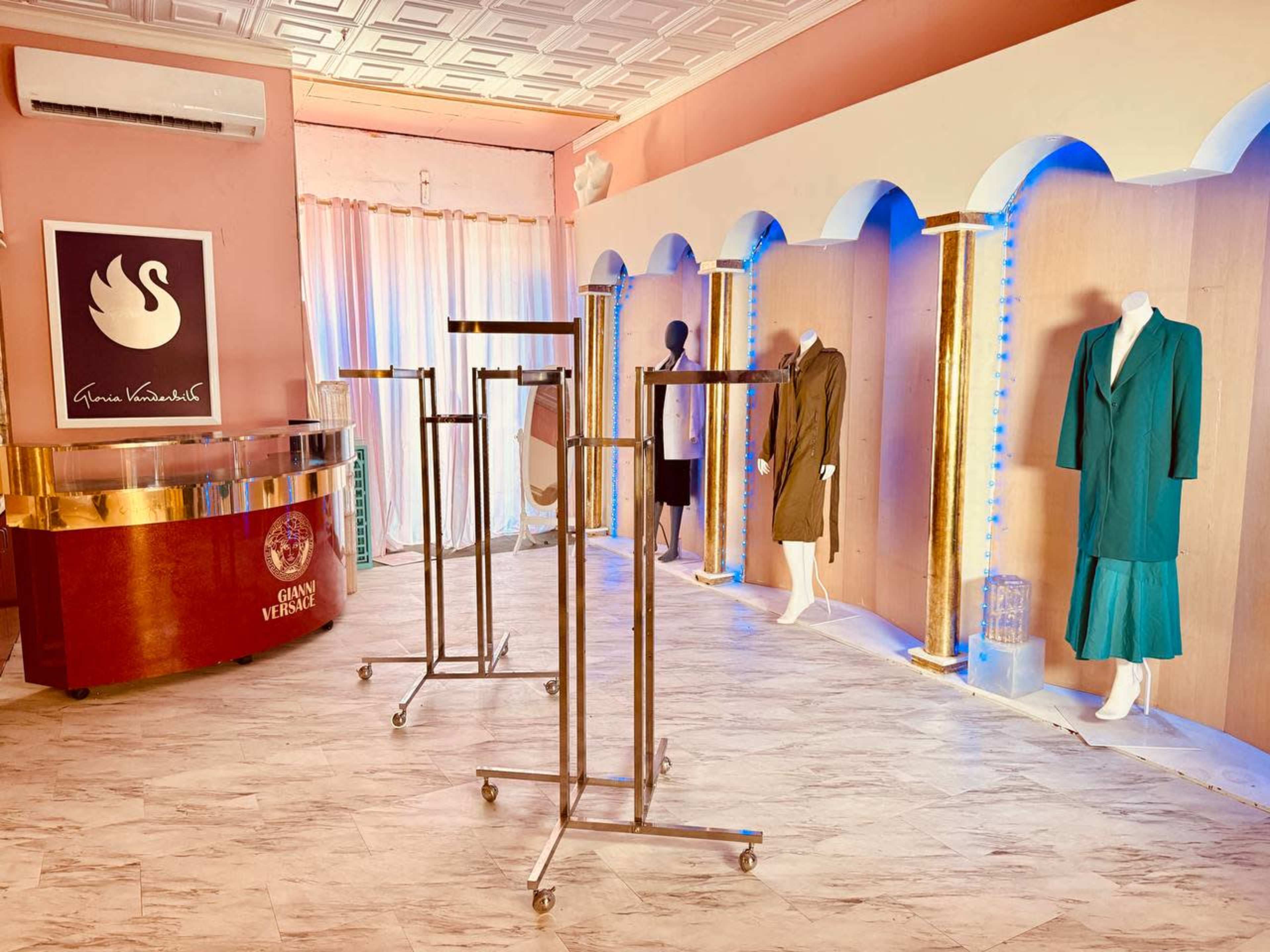 The image shows a boutique interior featuring clothing displays, a reception counter, and mannequins dressed in various outfits against a softly lit background.