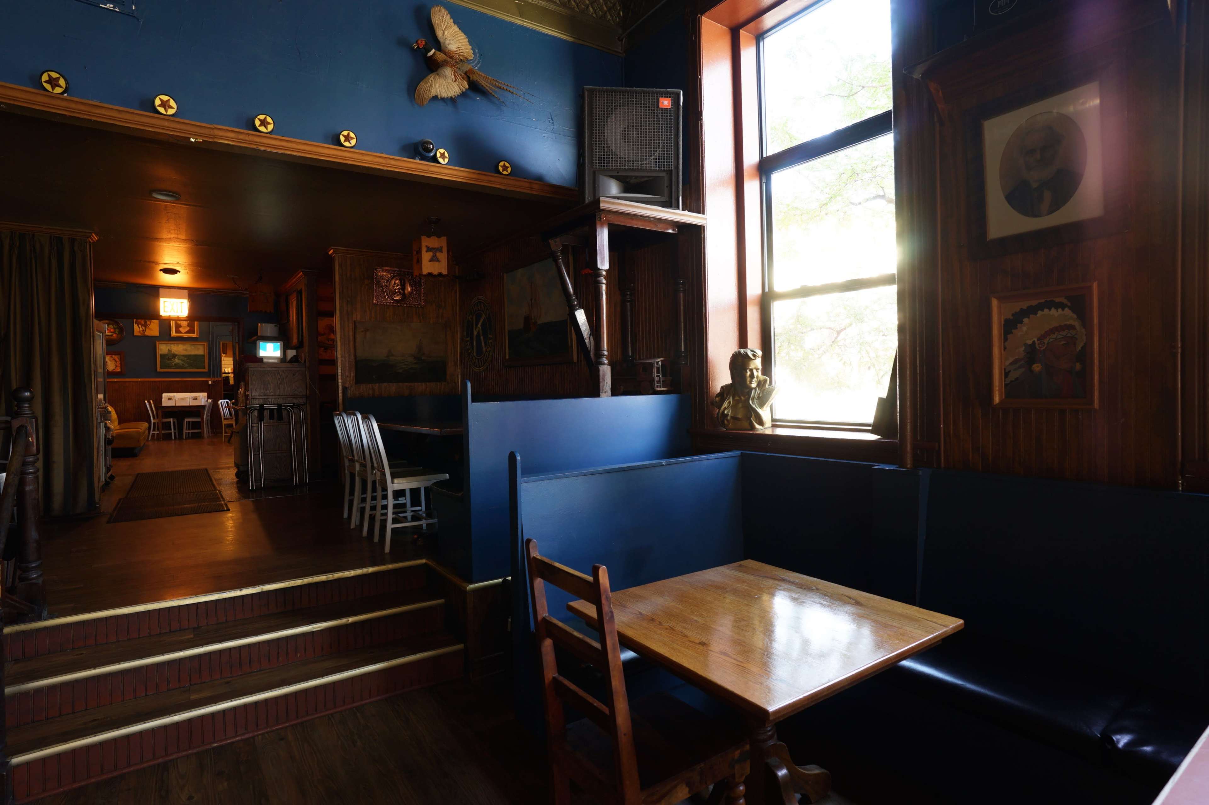 The image depicts a cozy interior of a bar or restaurant featuring dark blue walls, wooden furniture, and various framed pictures on the walls.