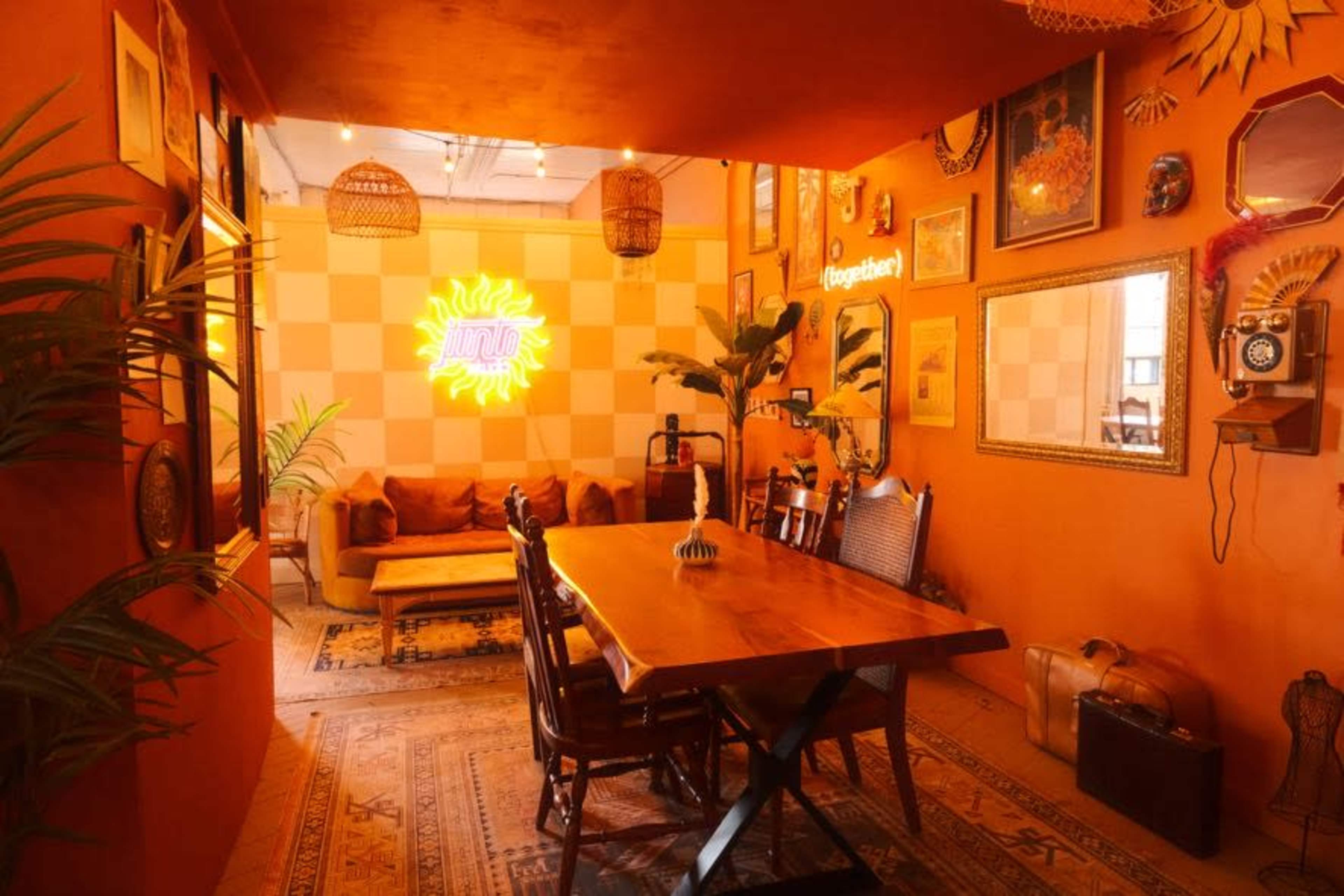 The image depicts a vibrant interior space with an orange color scheme, featuring a wooden dining table, a cozy seating area, and decorative wall art.
