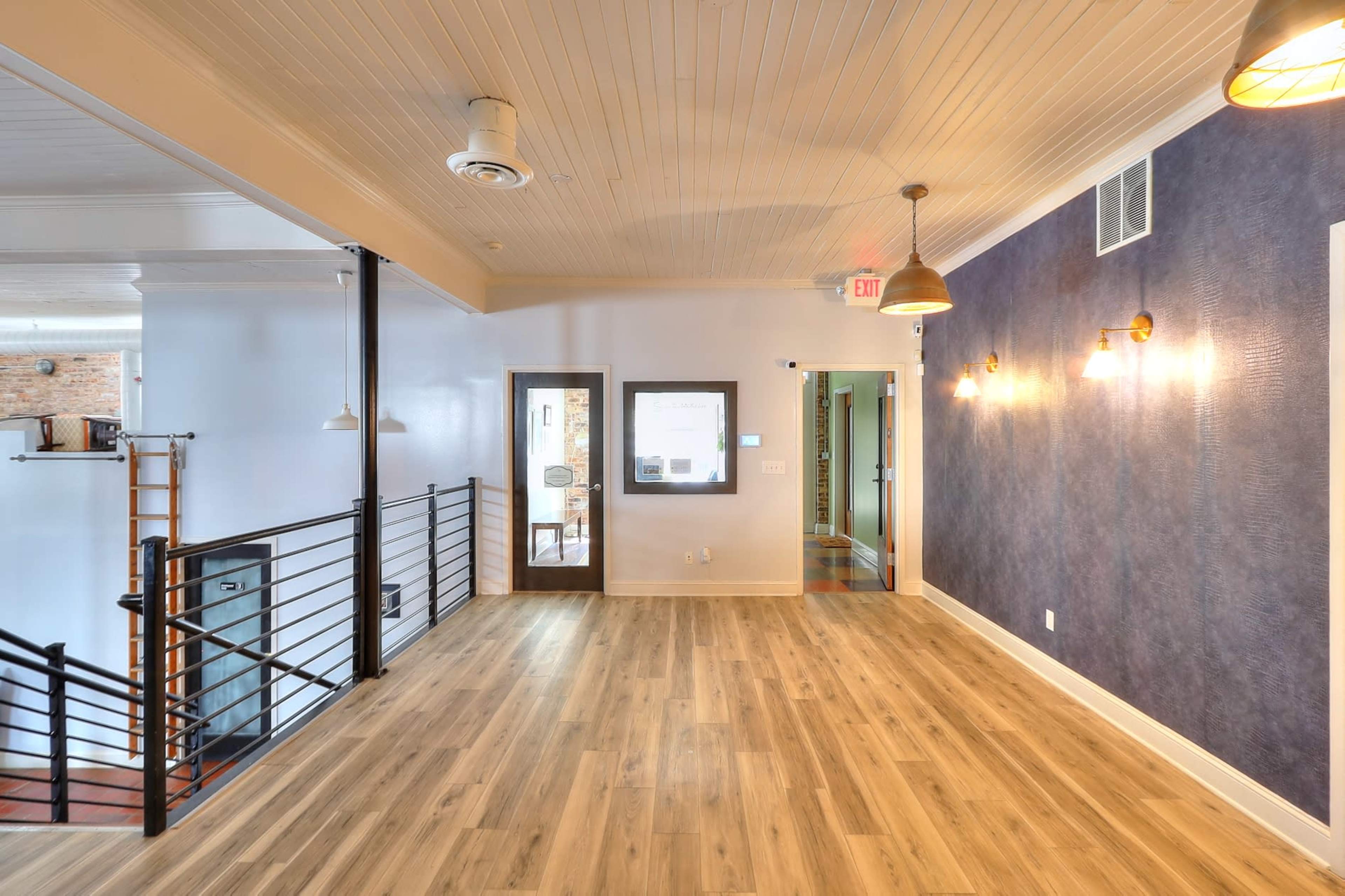 A spacious interior with wooden flooring, a blue accent wall, and various light fixtures, along with doors leading to other rooms.