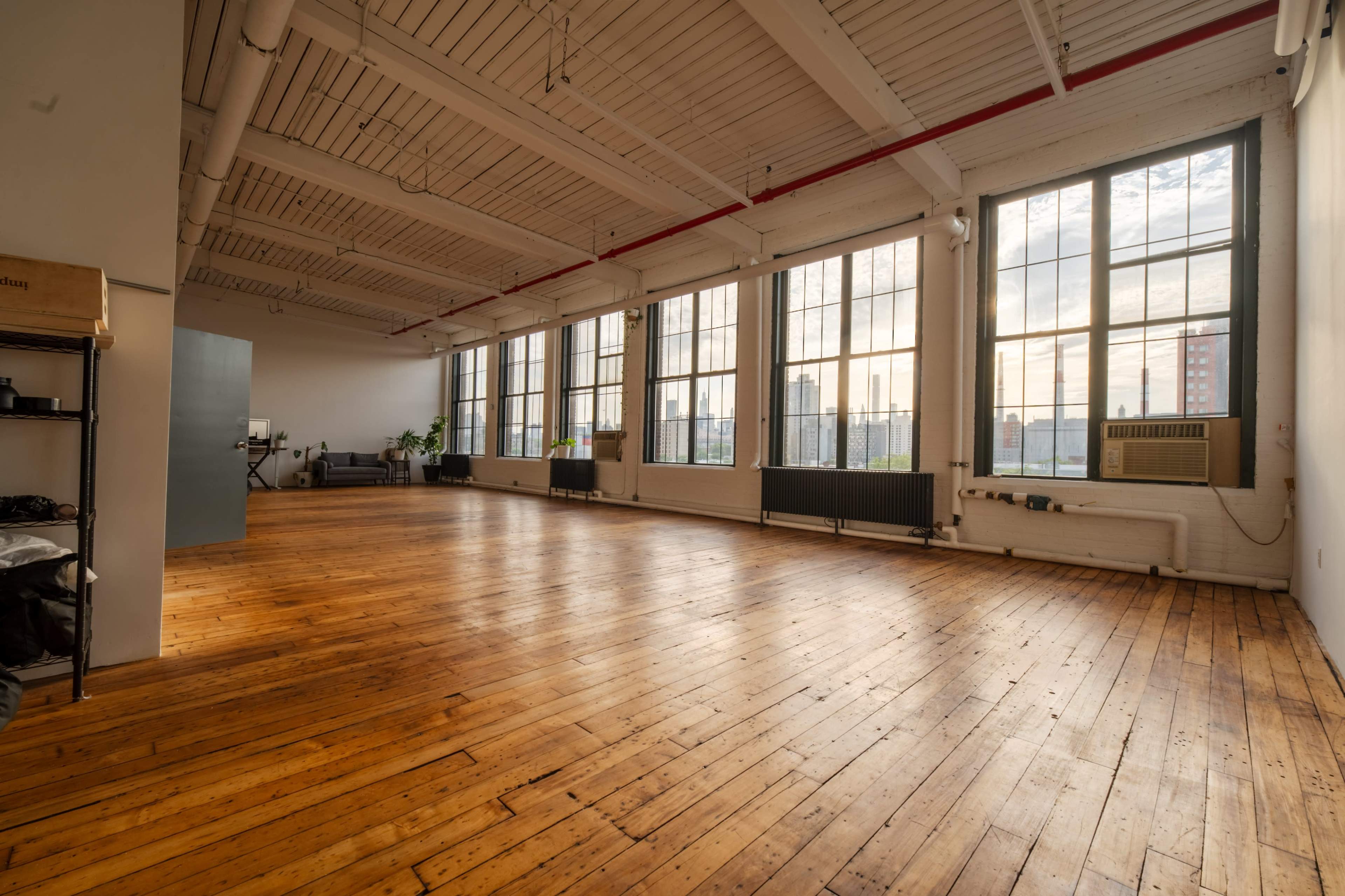 The image shows a spacious interior with large windows, wooden floors, and visible cityscape beyond the glass.