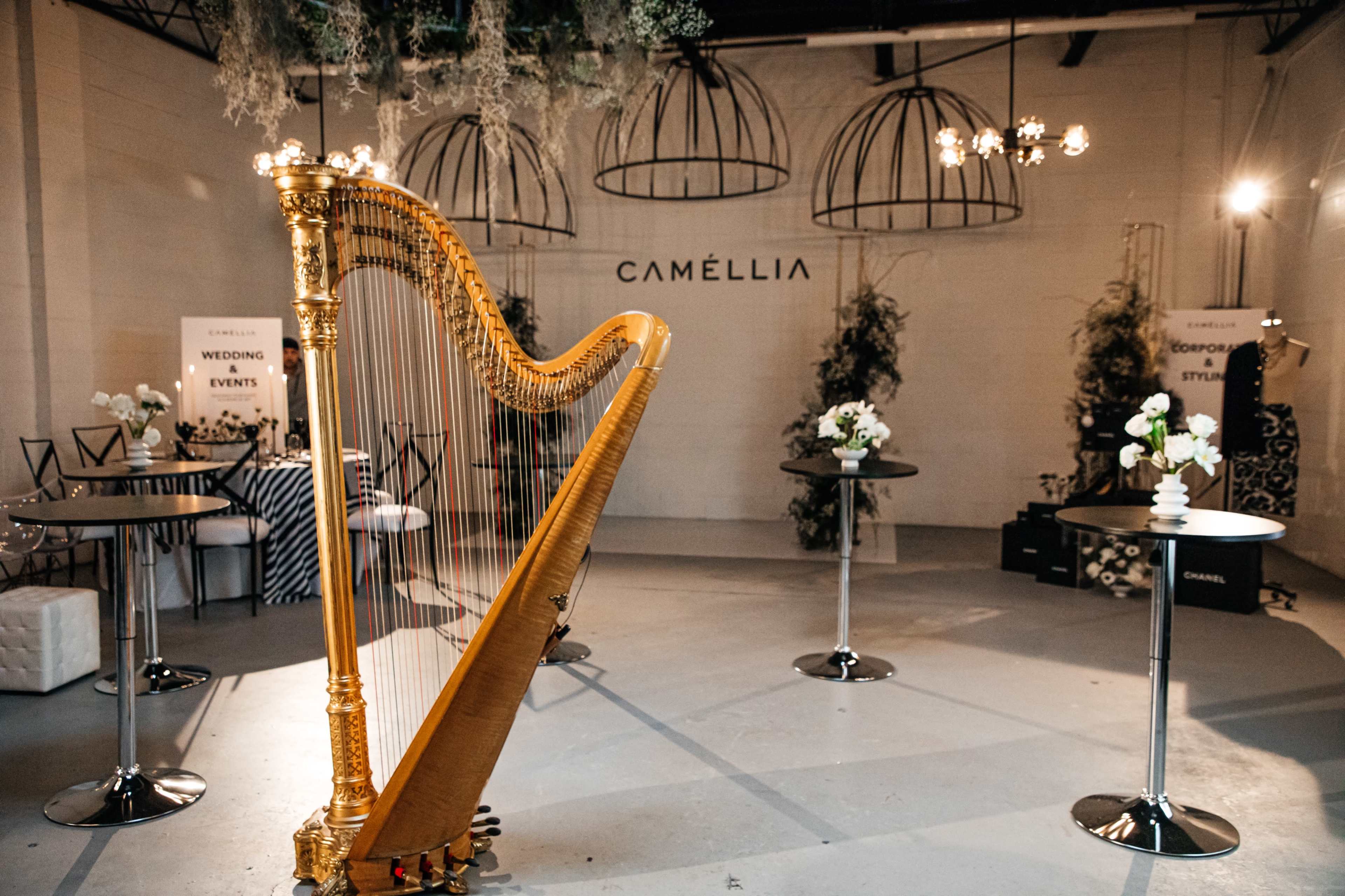 A gold harp stands prominently in a well-lit event space, surrounded by tables adorned with floral arrangements.