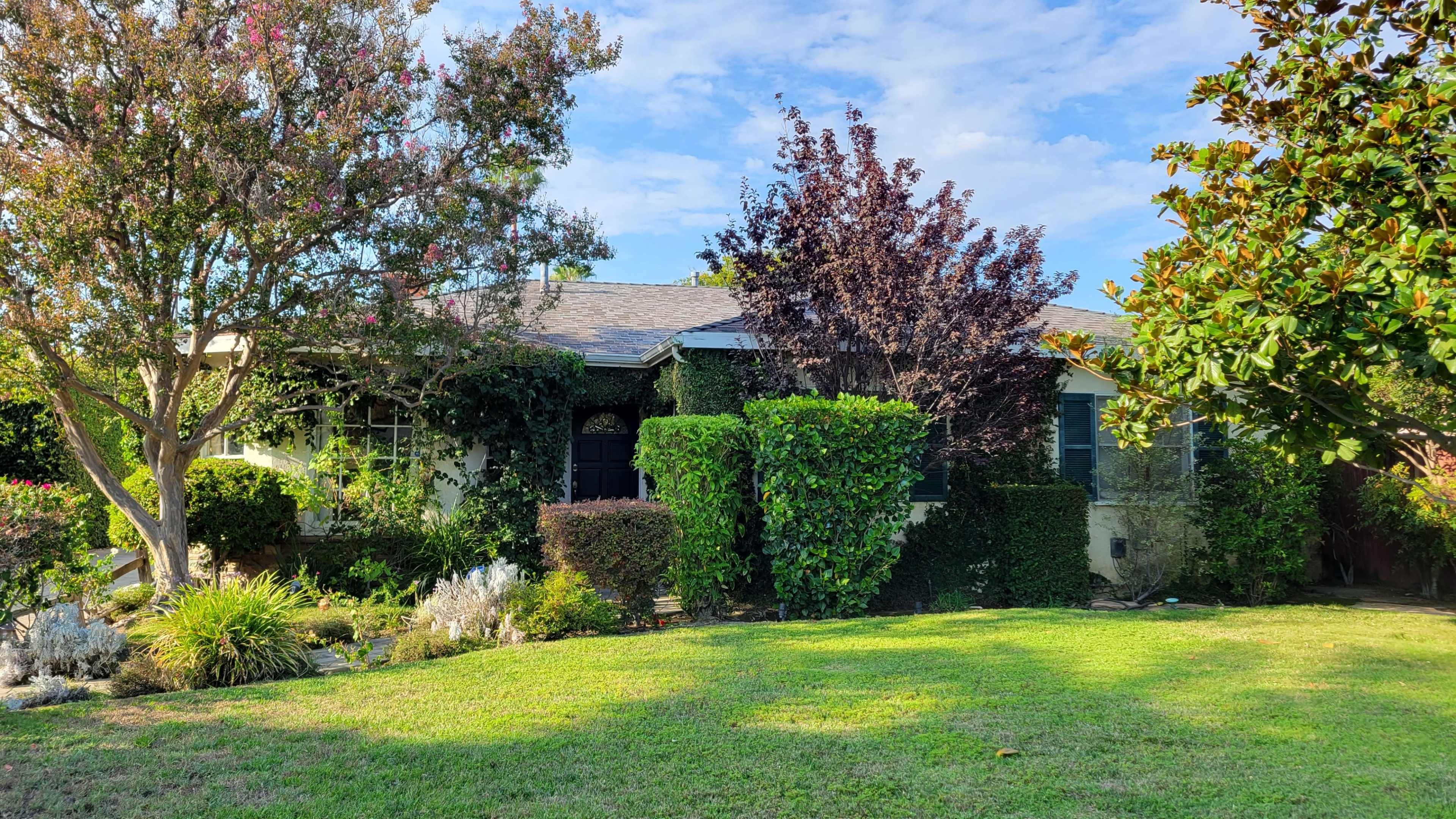 A house surrounded by various shrubs and trees, with a well-maintained lawn in front.