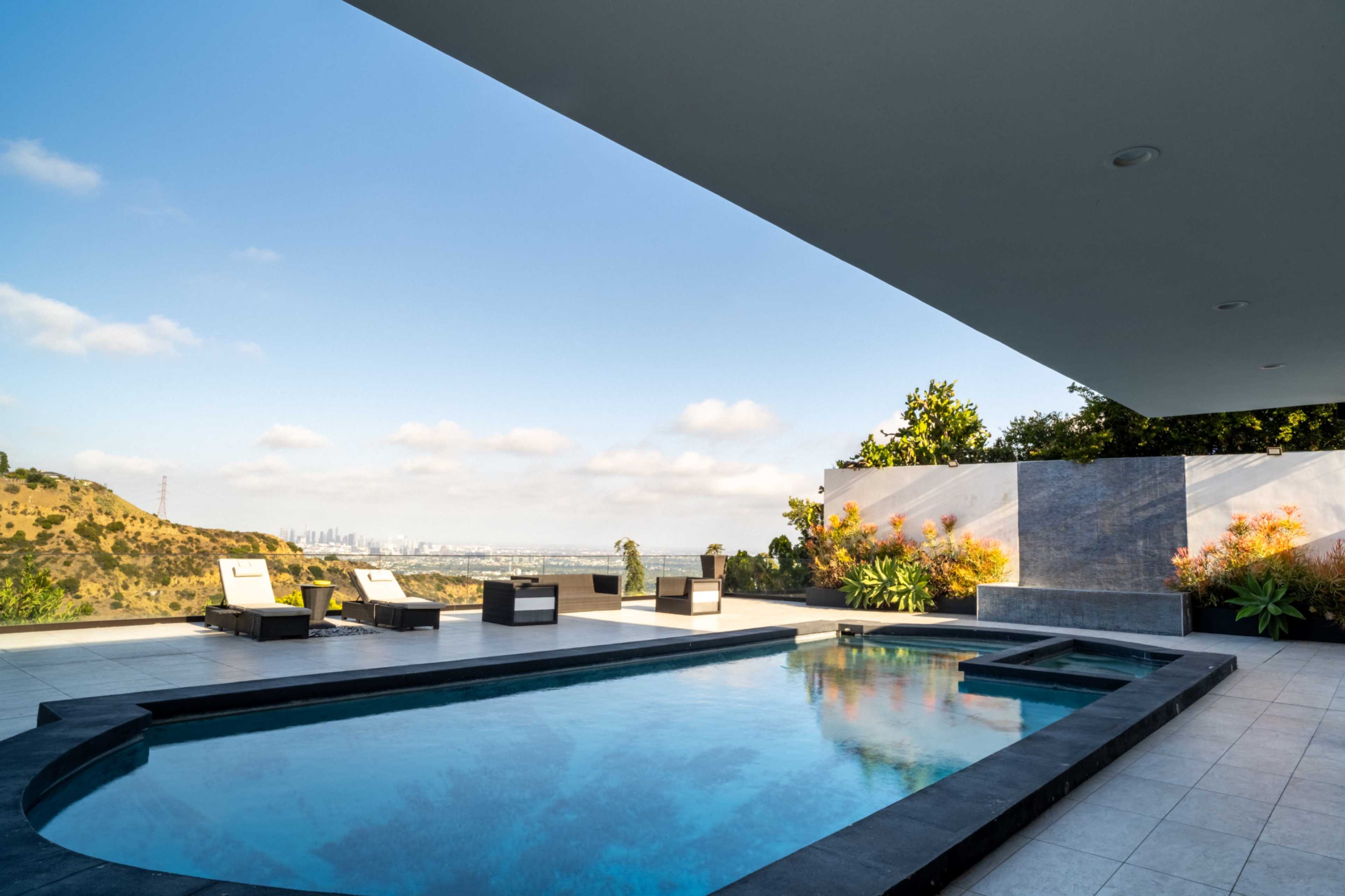 A modern patio features a swimming pool surrounded by lounge chairs and views of a distant cityscape.