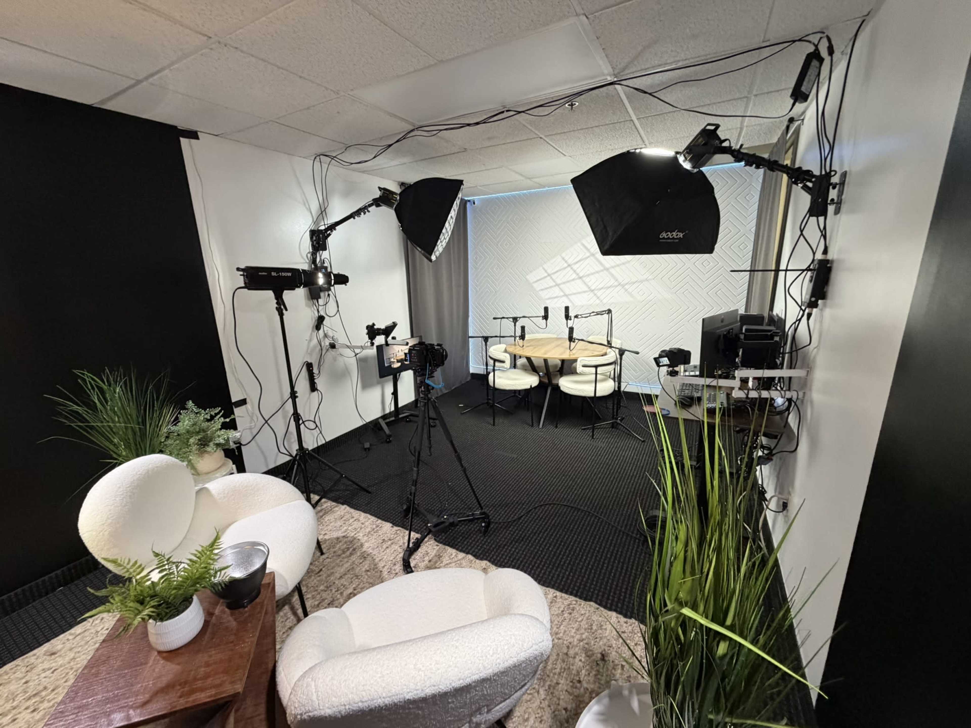 The image shows a professional studio setup with two lights, a camera, and a round table surrounded by chairs, all placed in a well-organized space.