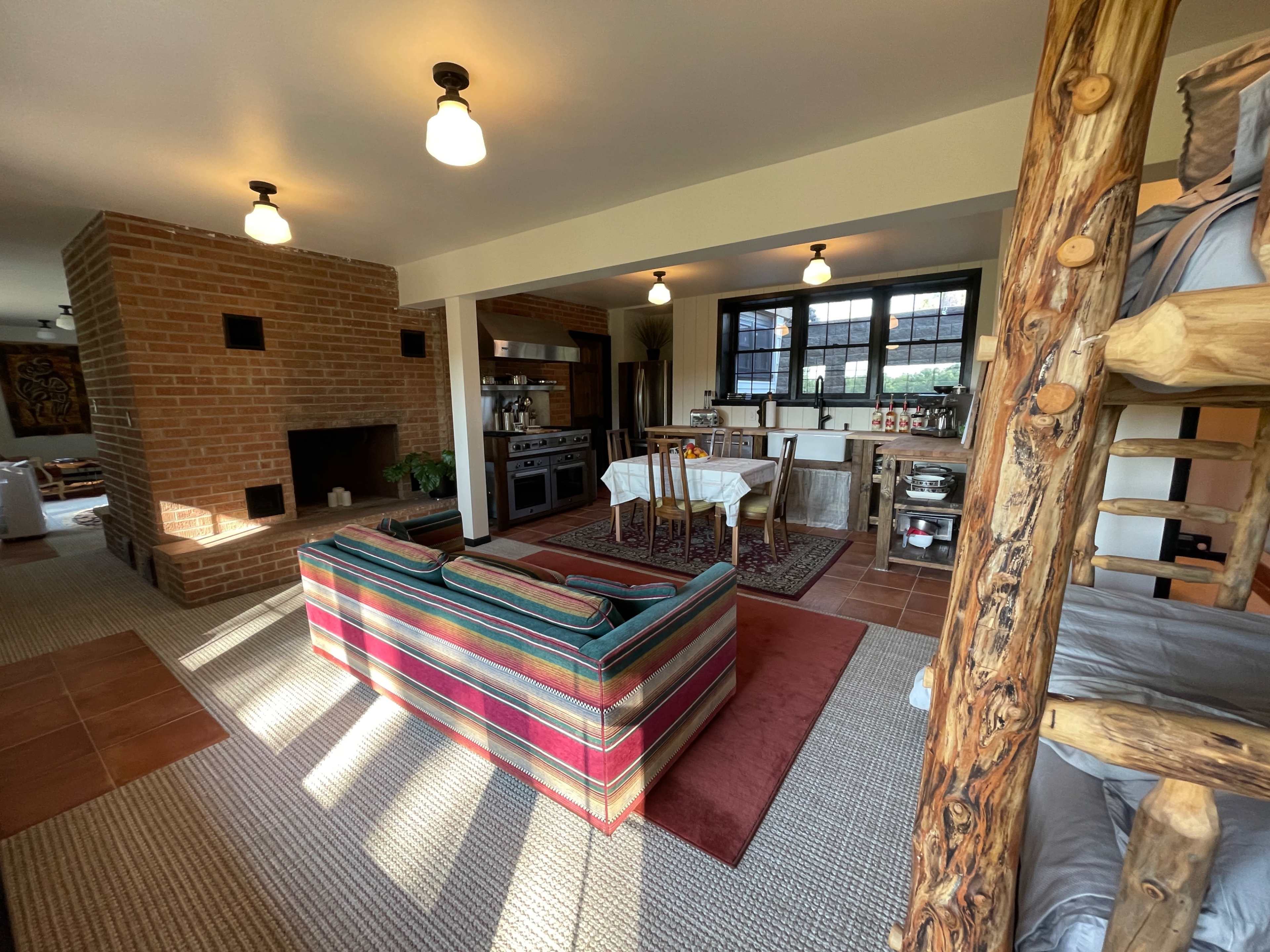 A cozy living space featuring a striped sofa, a brick fireplace, a wooden dining area, and a kitchen in an open-concept layout.