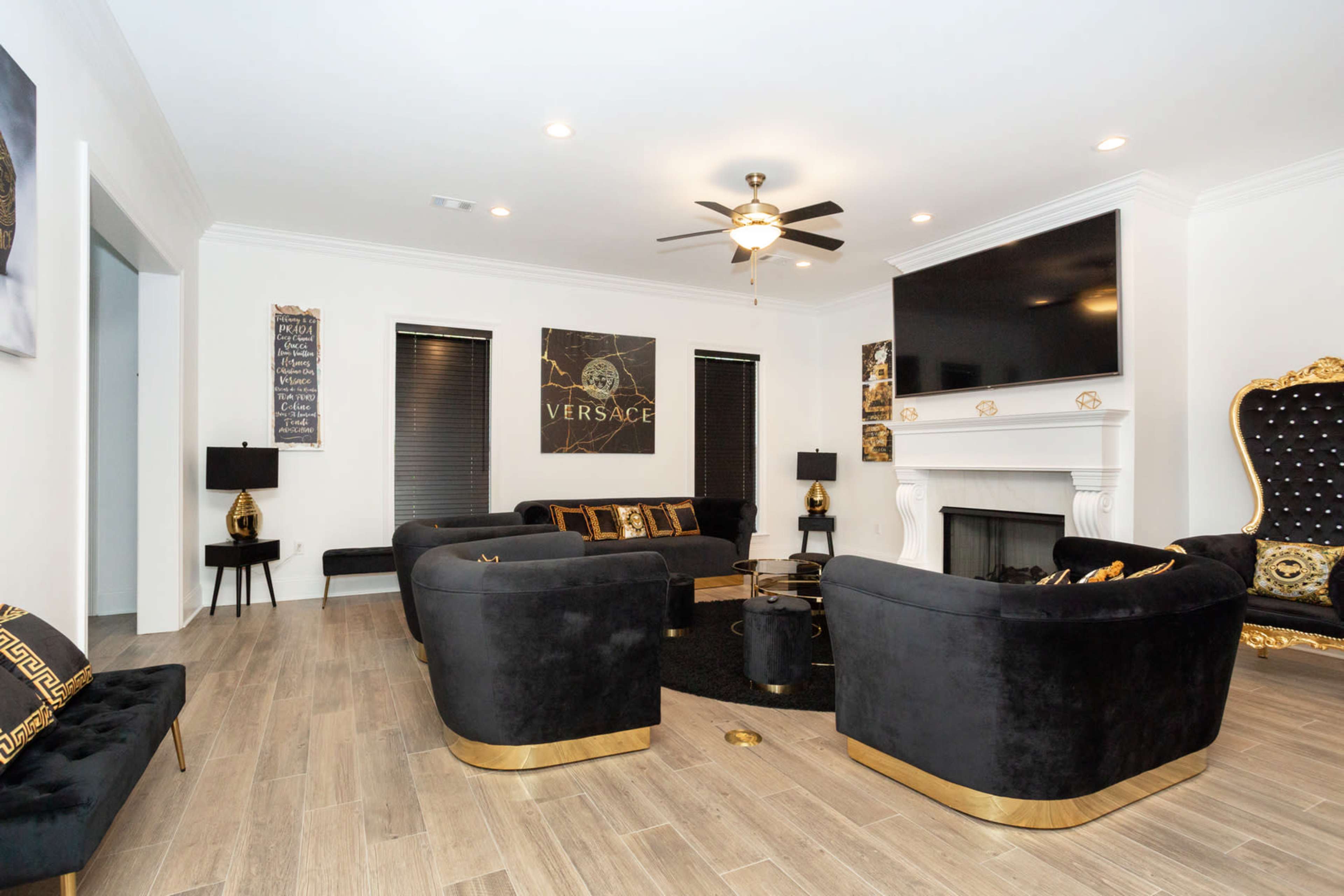 The living room features black velvet furniture with gold accents, a large flat-screen television, and a decorative fireplace.
