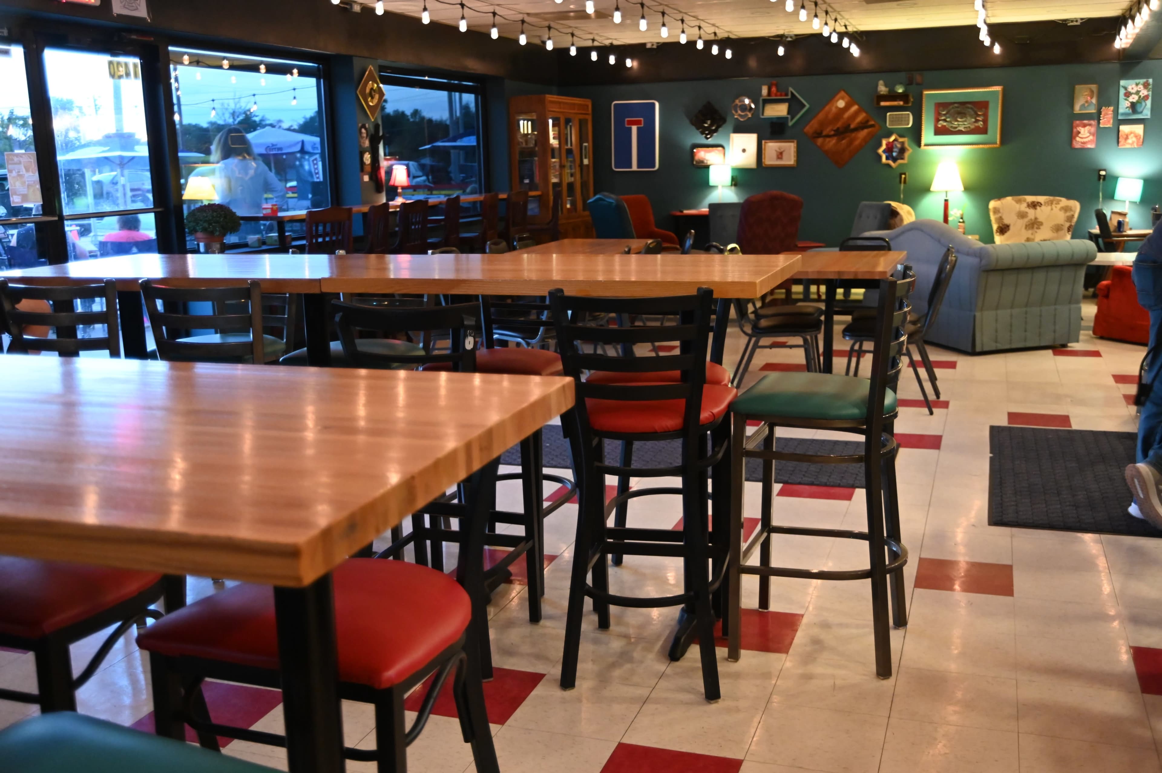 The image shows a cozy café interior with wooden tables and high chairs, dim lighting, and colorful seating areas along the walls.