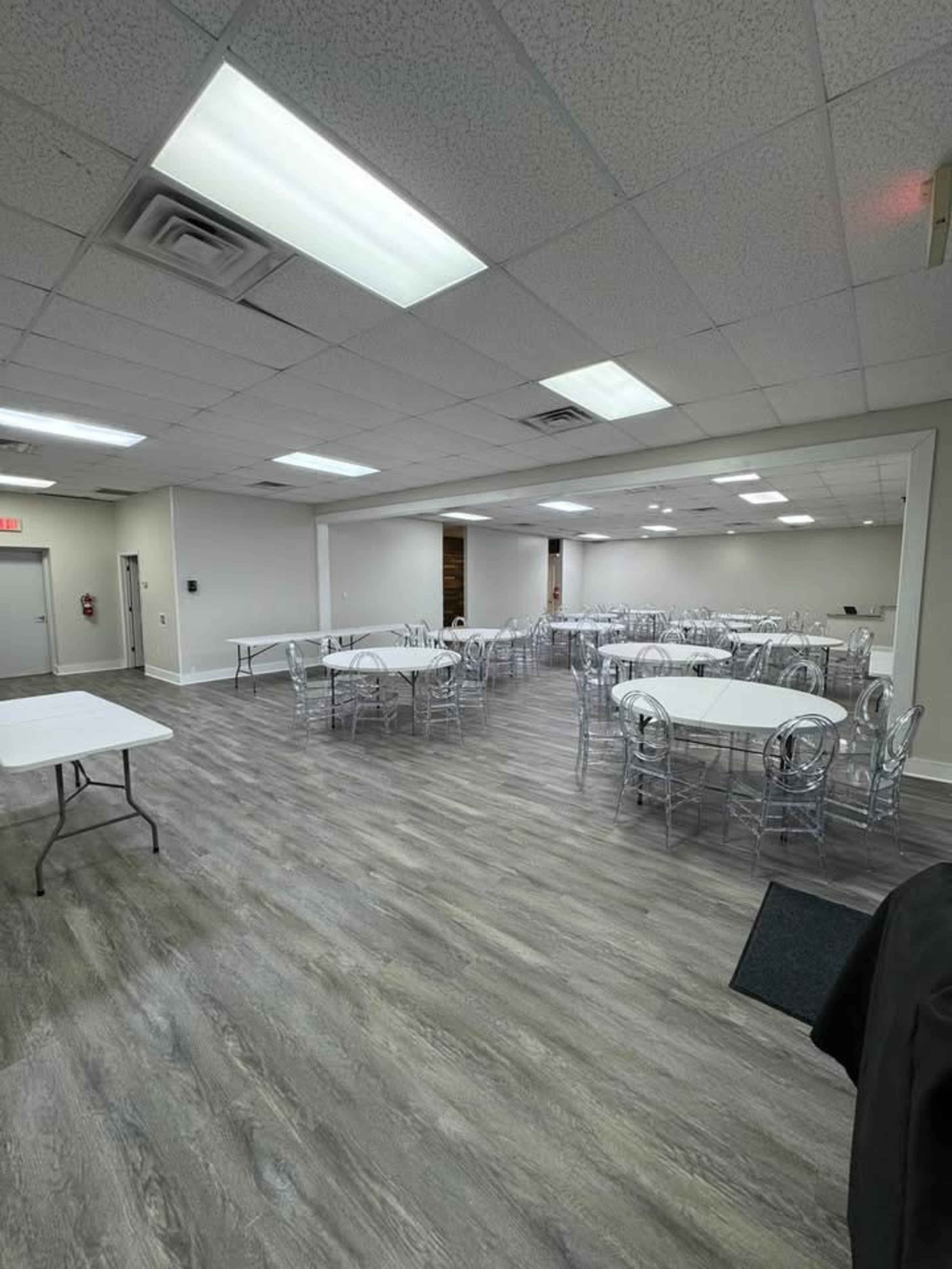 The image shows a spacious, well-lit room with several round tables and chairs arranged throughout, along with a few empty rectangular tables along the sides.