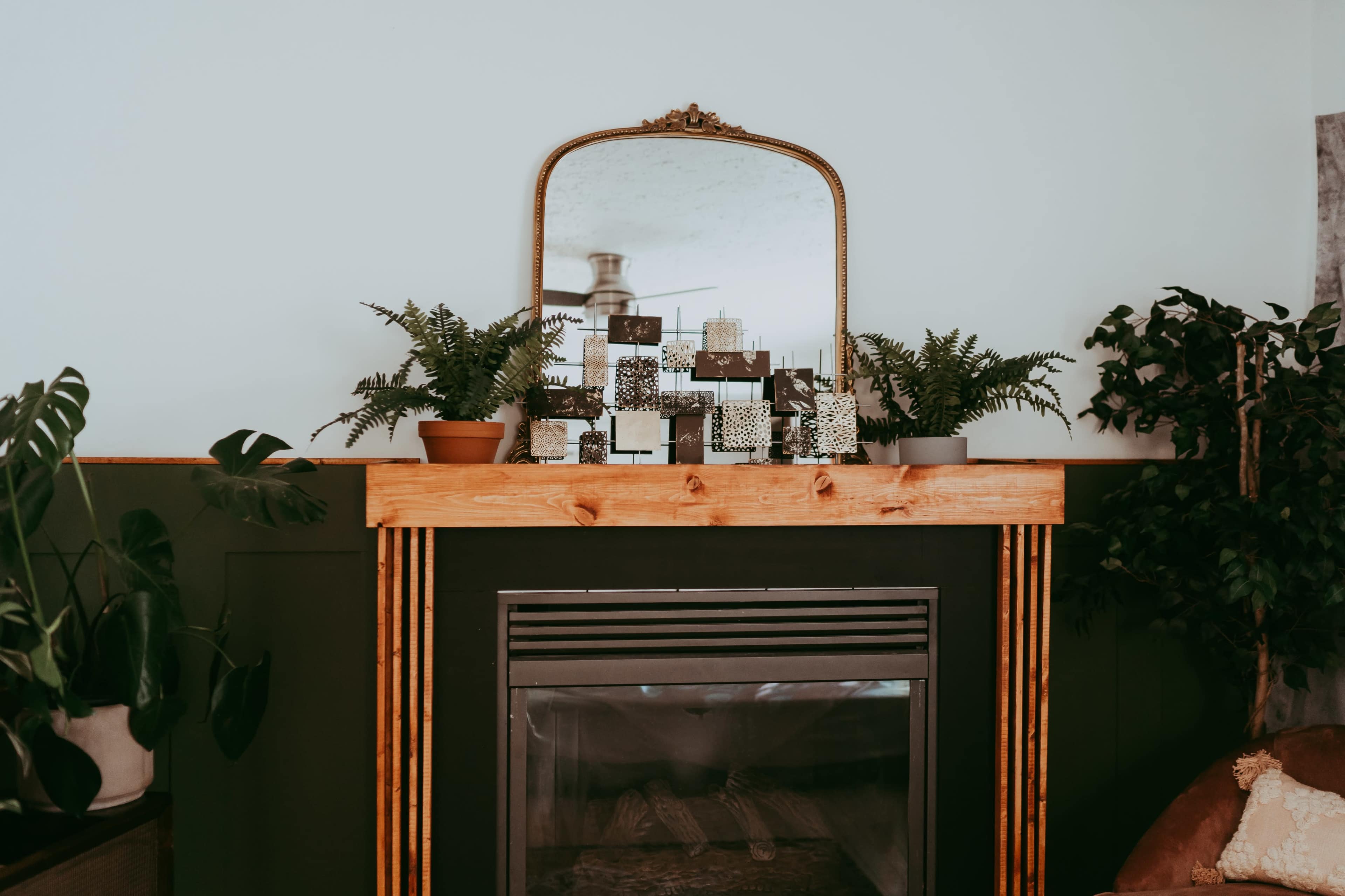 A fireplace mantel is adorned with plants and decorative items, and a mirror hangs above it.