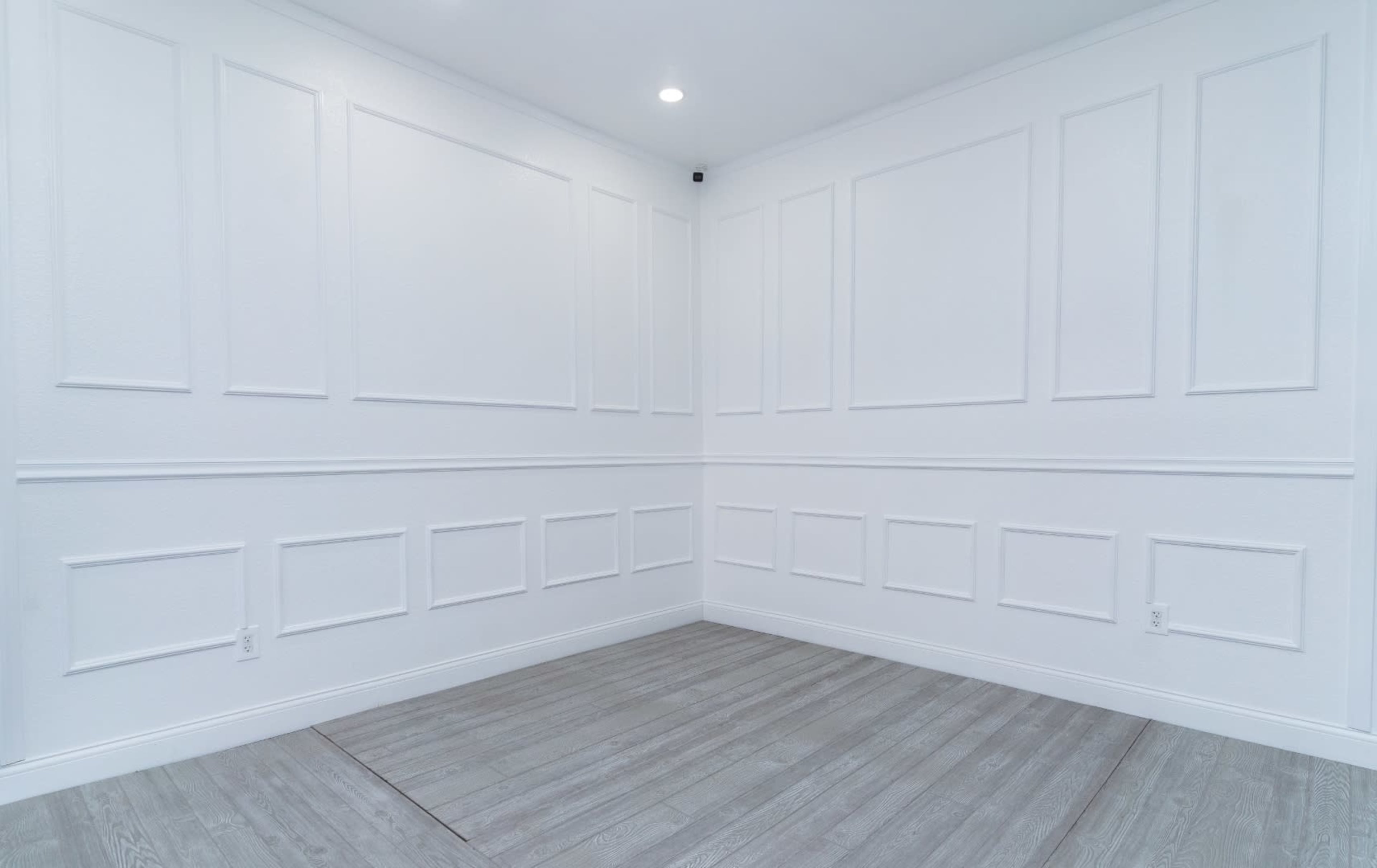 The image shows a empty room with white walls featuring decorative paneling and a light-colored floor.