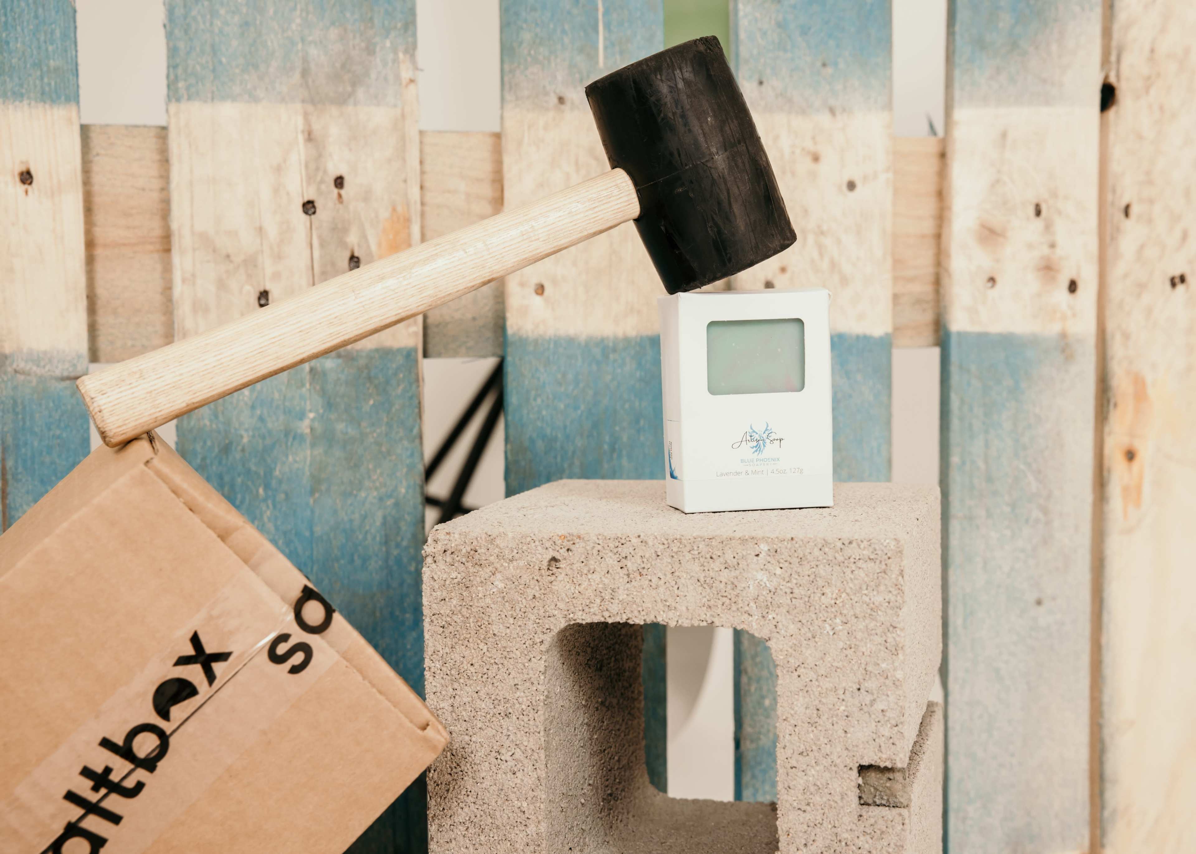 A rubber mallet rests on a small white device placed on a concrete block, next to a cardboard box.