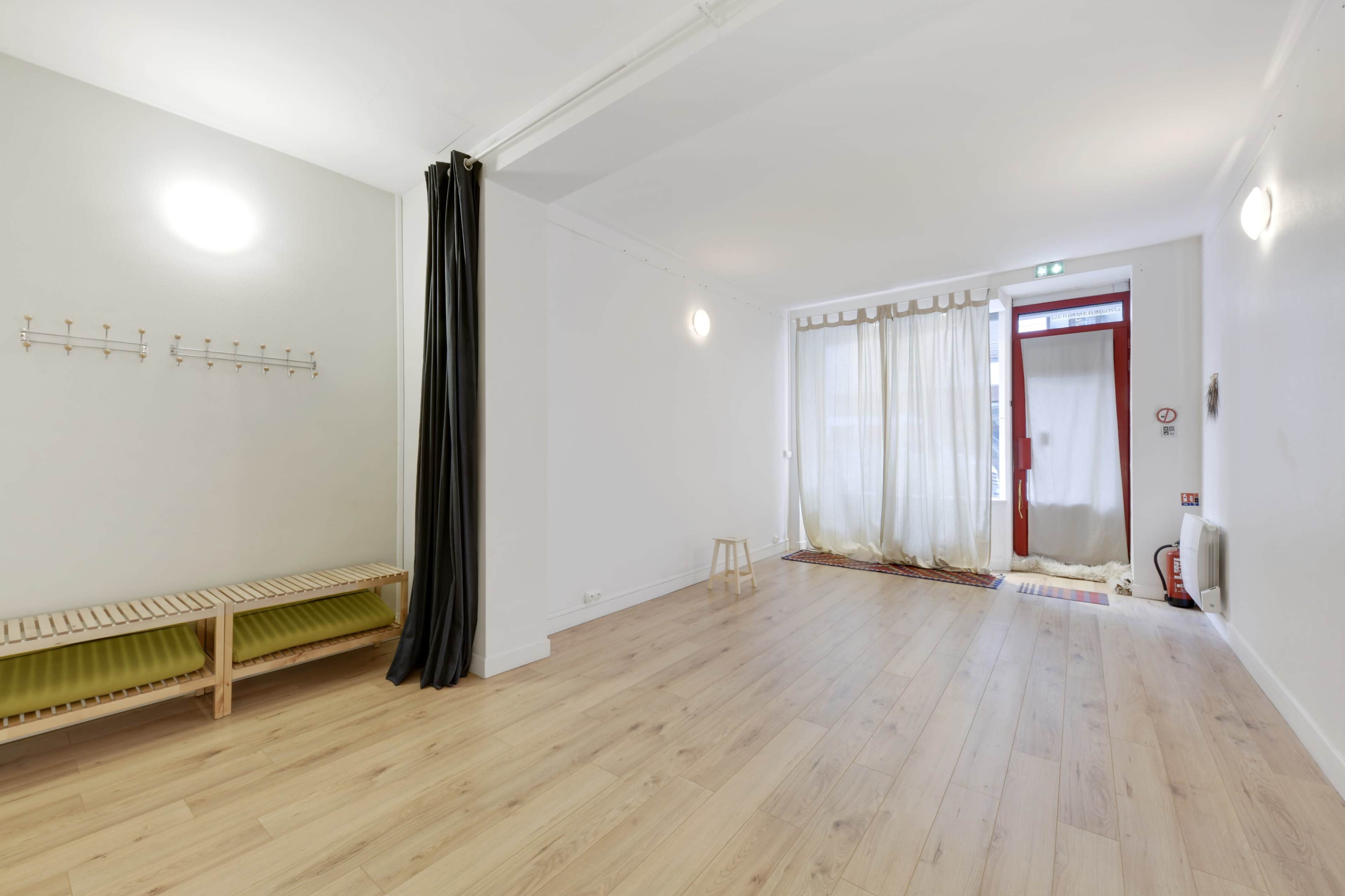 A spacious, minimally furnished room with wooden flooring, a bench along one wall, and sheer curtains covering a doorway.