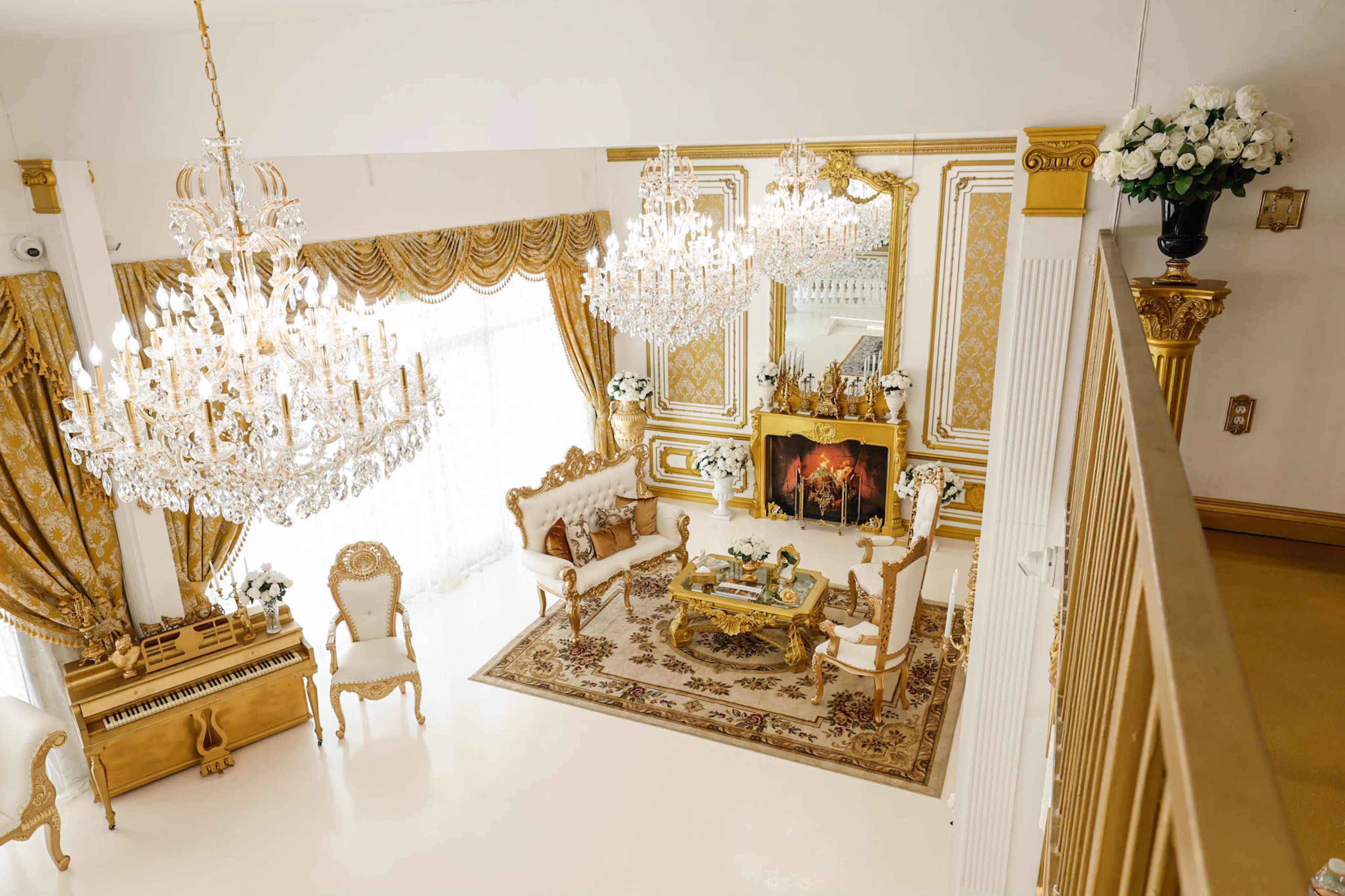 An elegantly decorated living room with golden accents, multiple chandeliers, and a lavish seating arrangement centered around a coffee table.