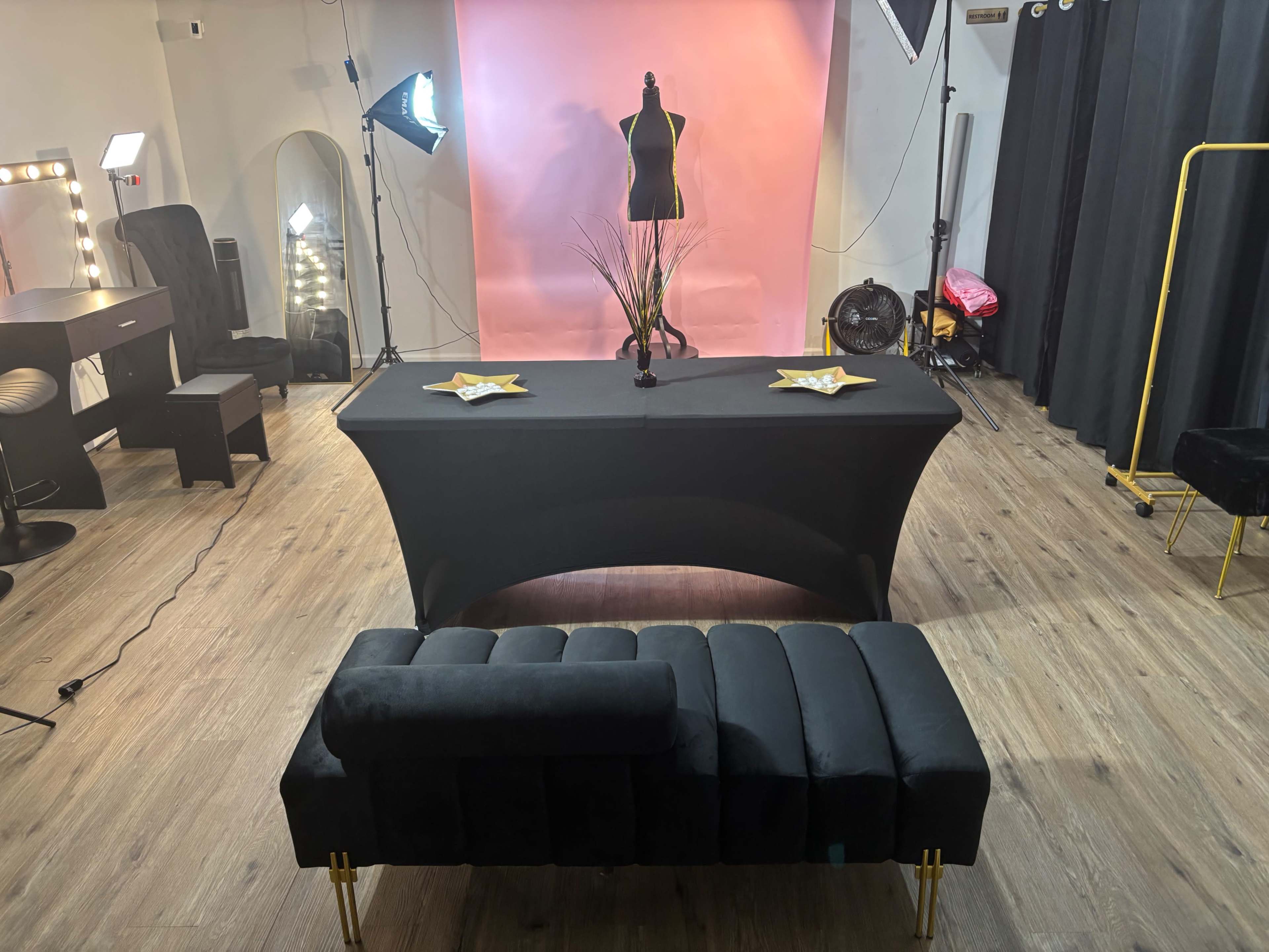 A photo studio setup features a black table with decorative items, a dress form, and professional lighting against a pink backdrop.