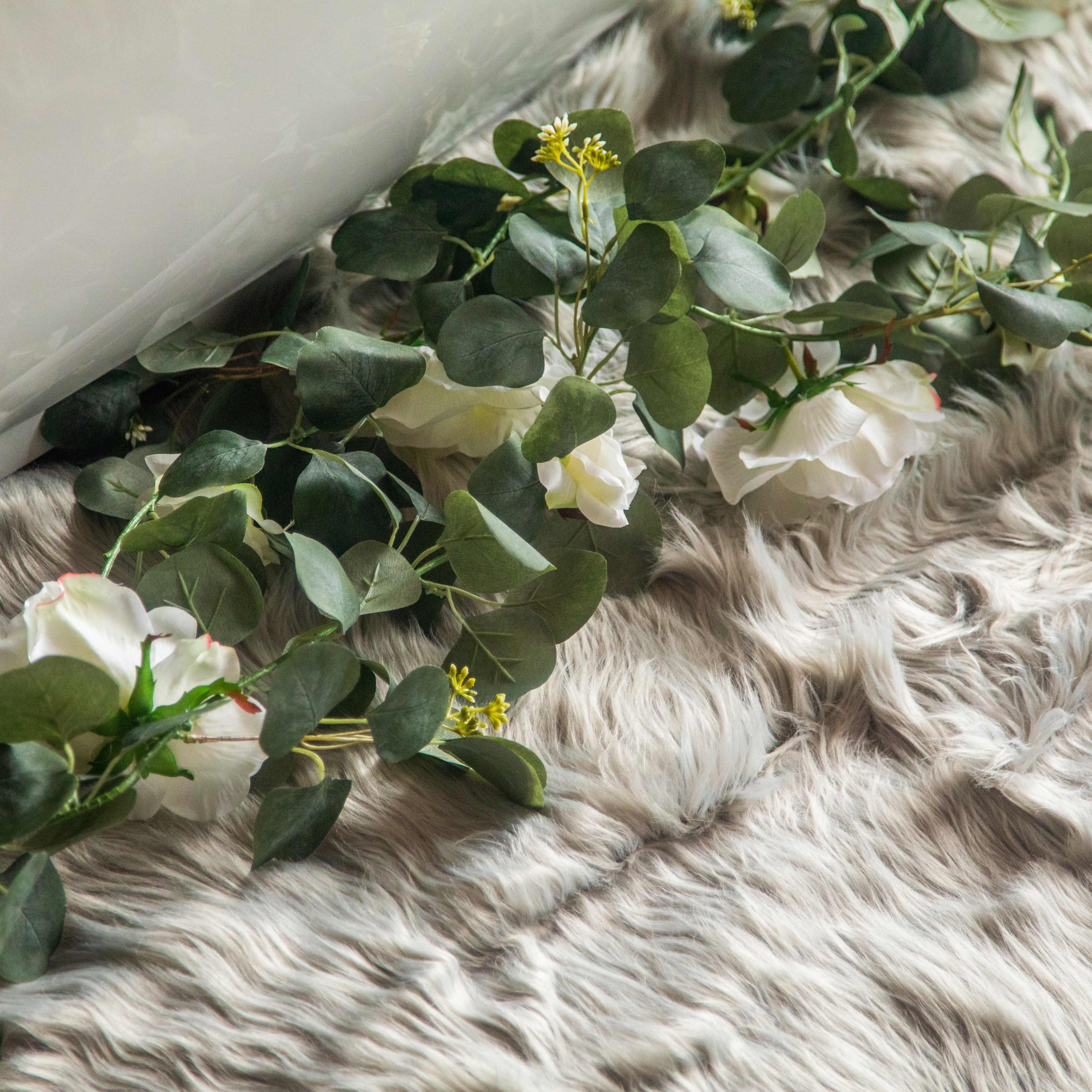 A garland of faux flowers and leaves lies on a textured fur rug.