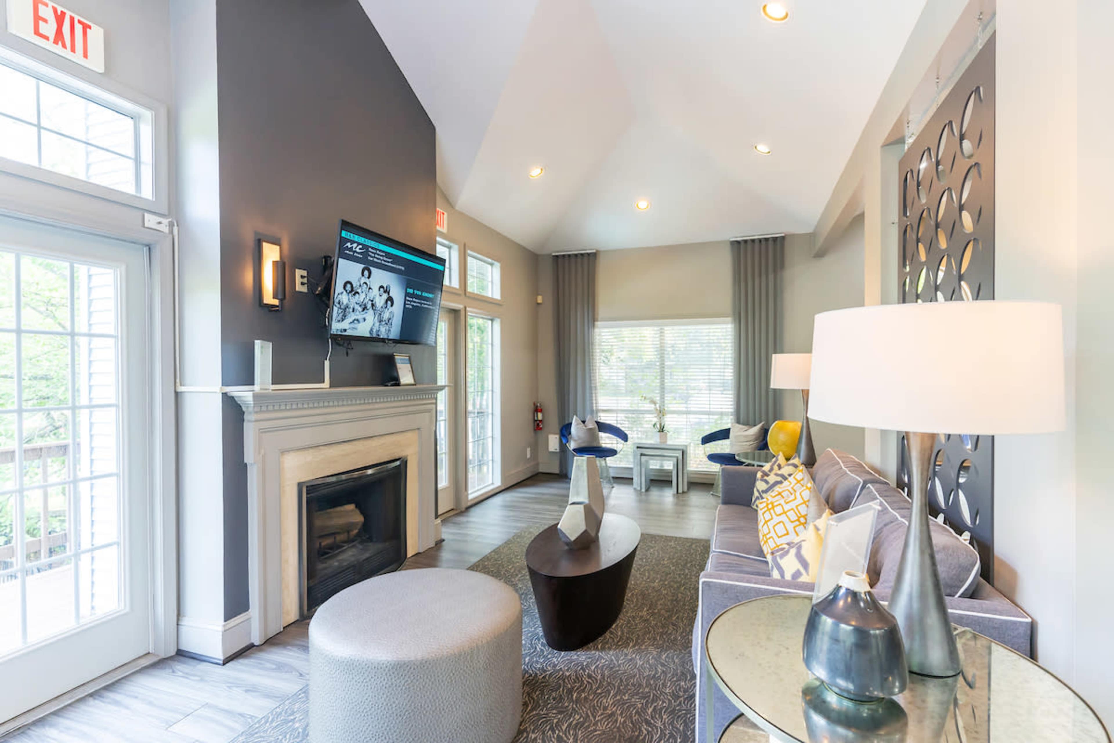 A modern lounge area with a fireplace, large windows, a television mounted on the wall, and comfortable seating arrangements.