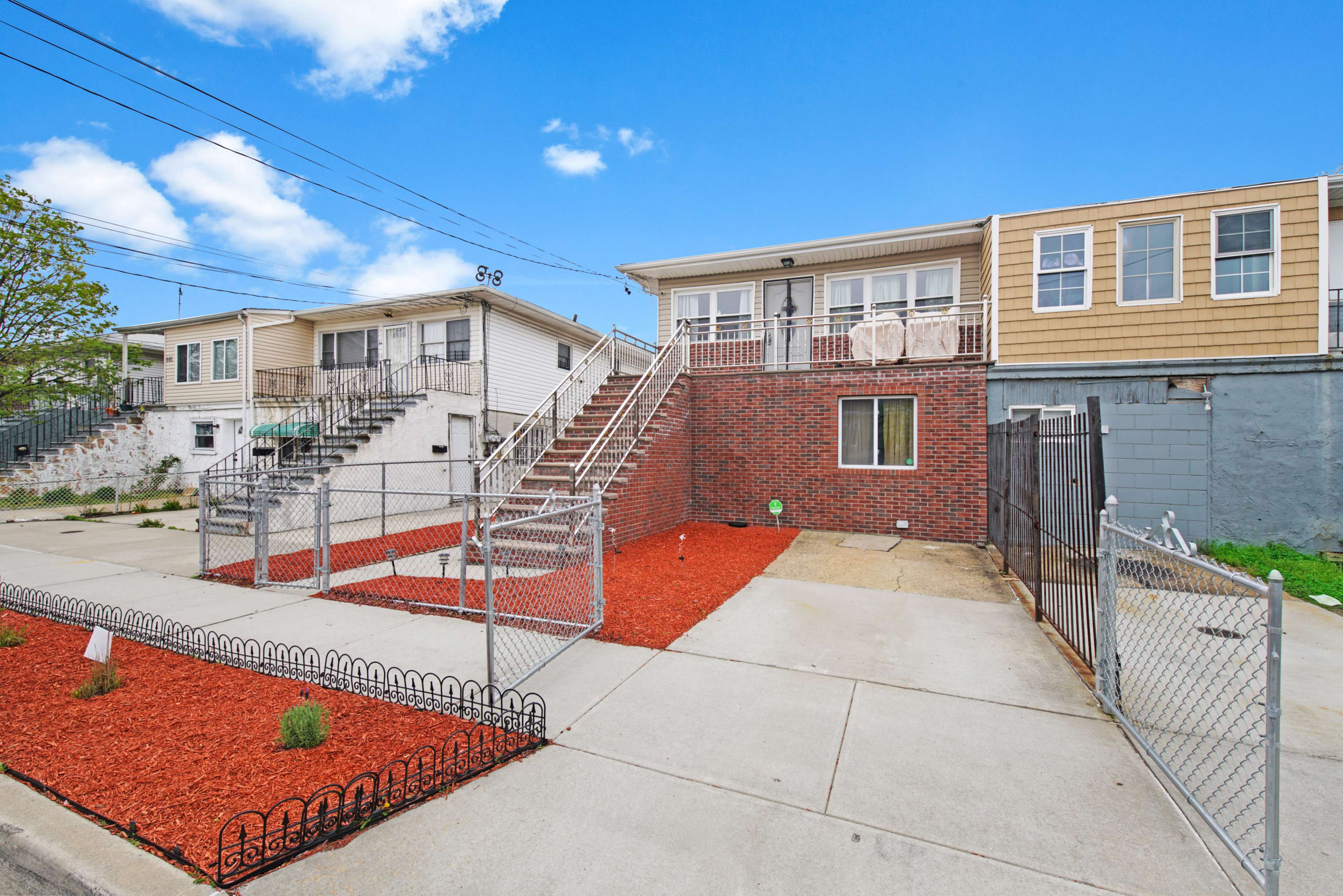 A multi-unit residential building with a fenced yard, featuring a brick facade and stairs leading to a front porch.