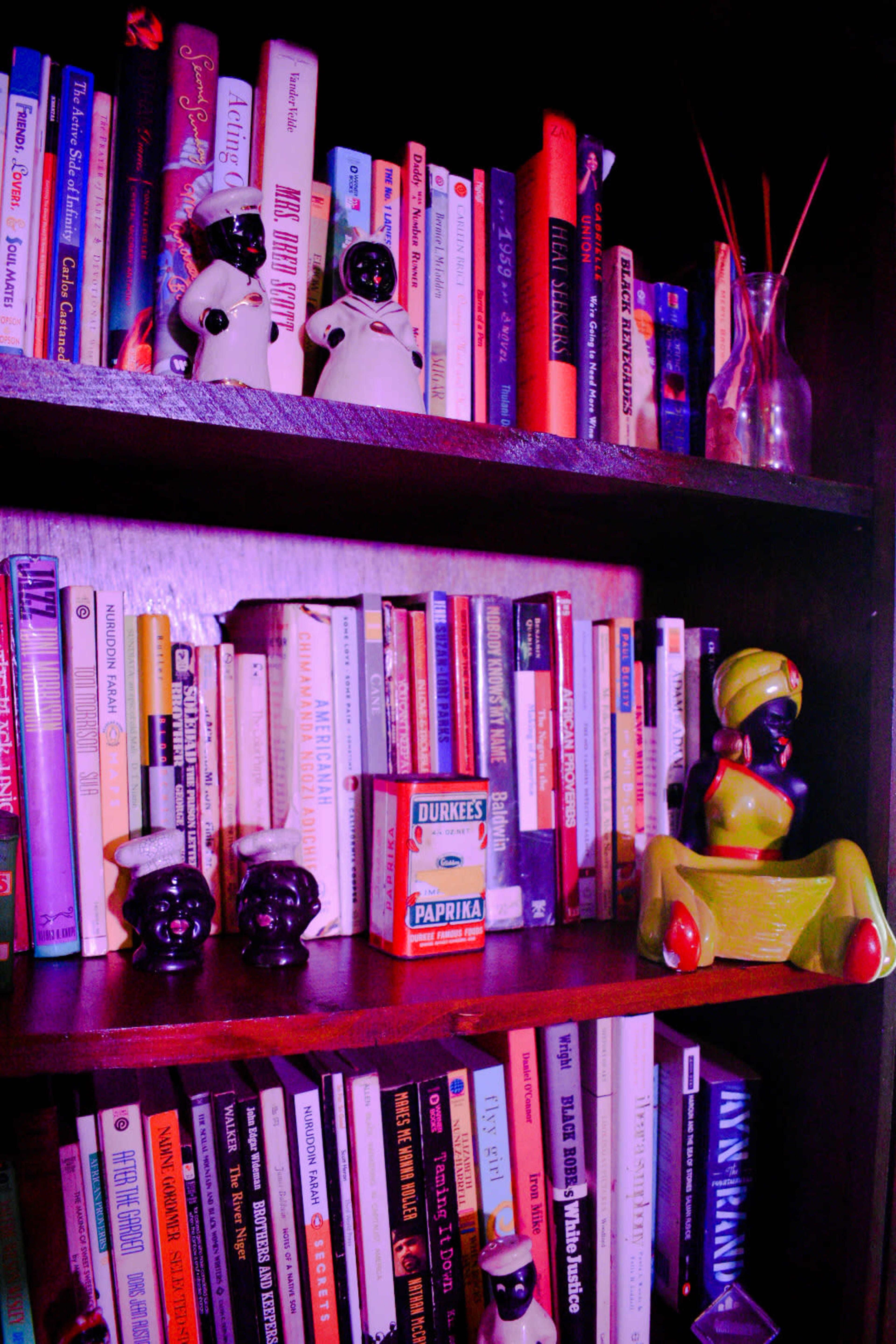 A bookshelf filled with various books, decorative figurines, and a red and white can of paprika.