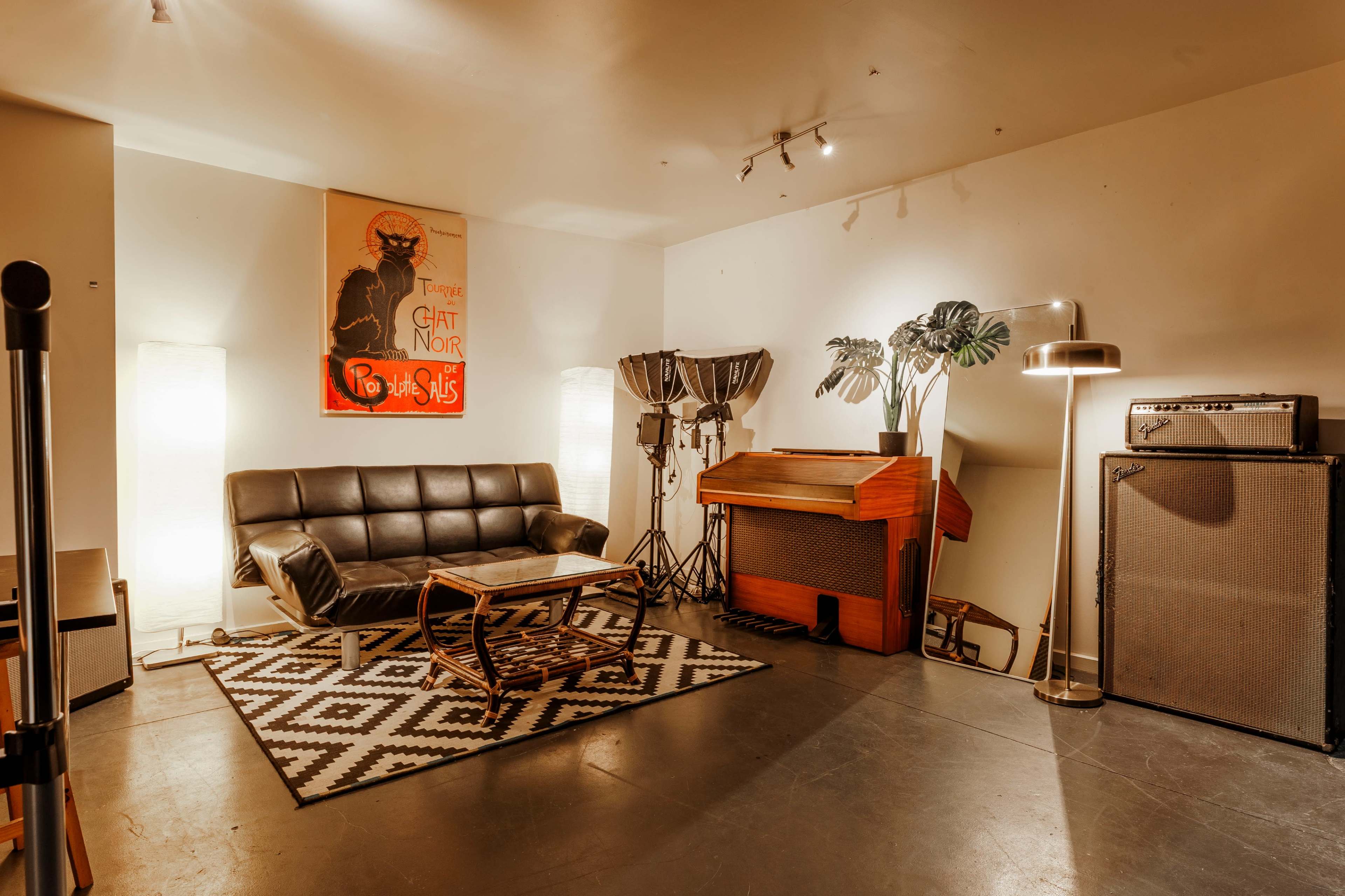The image shows a stylish music room featuring a black leather sofa, a vintage keyboard, an amplifier, and decorative plants against a minimalist backdrop.
