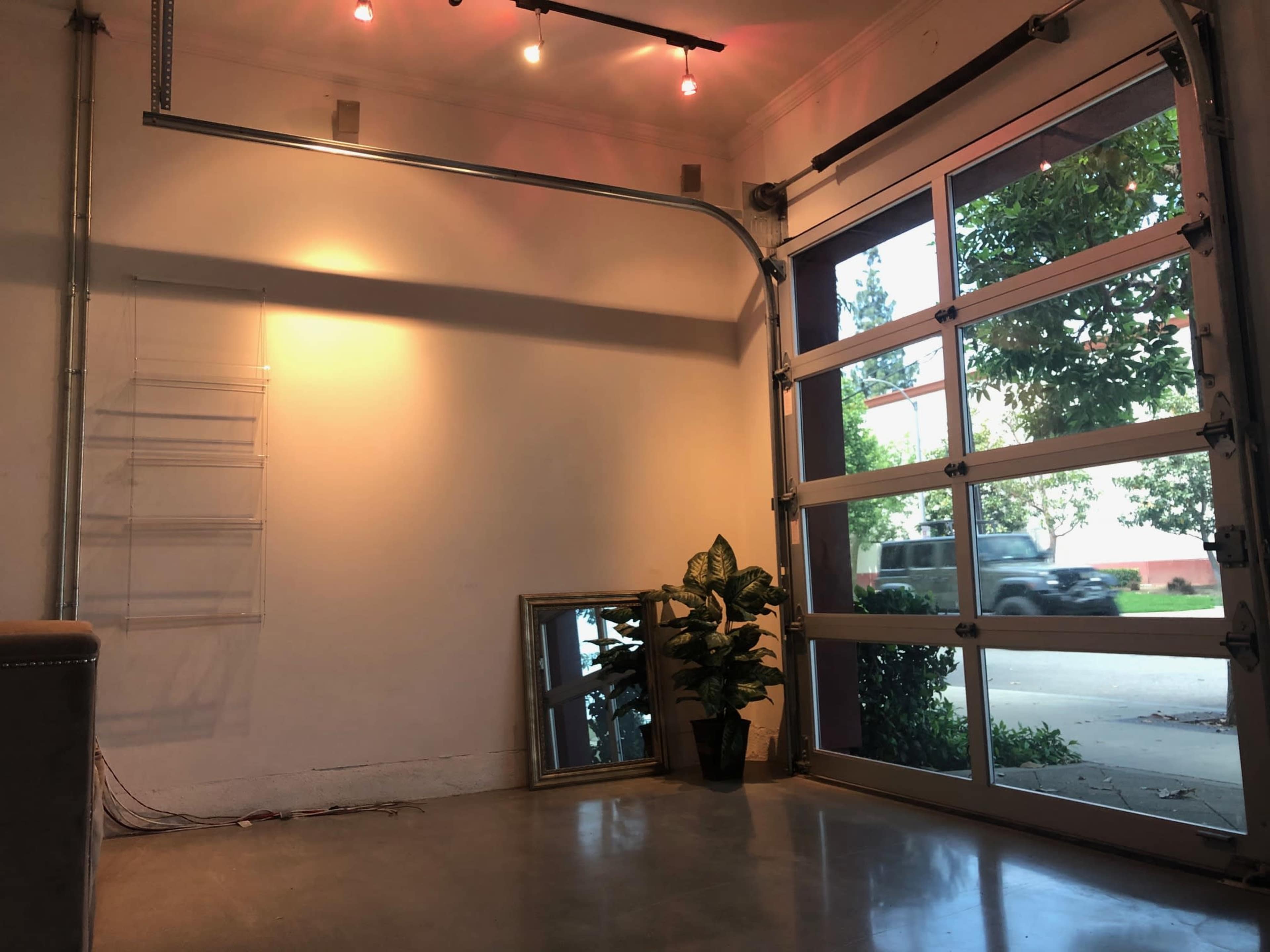 A modern garage space features a large glass door, a potted plant, and a mirror against the wall, with soft lighting illuminating the interior.