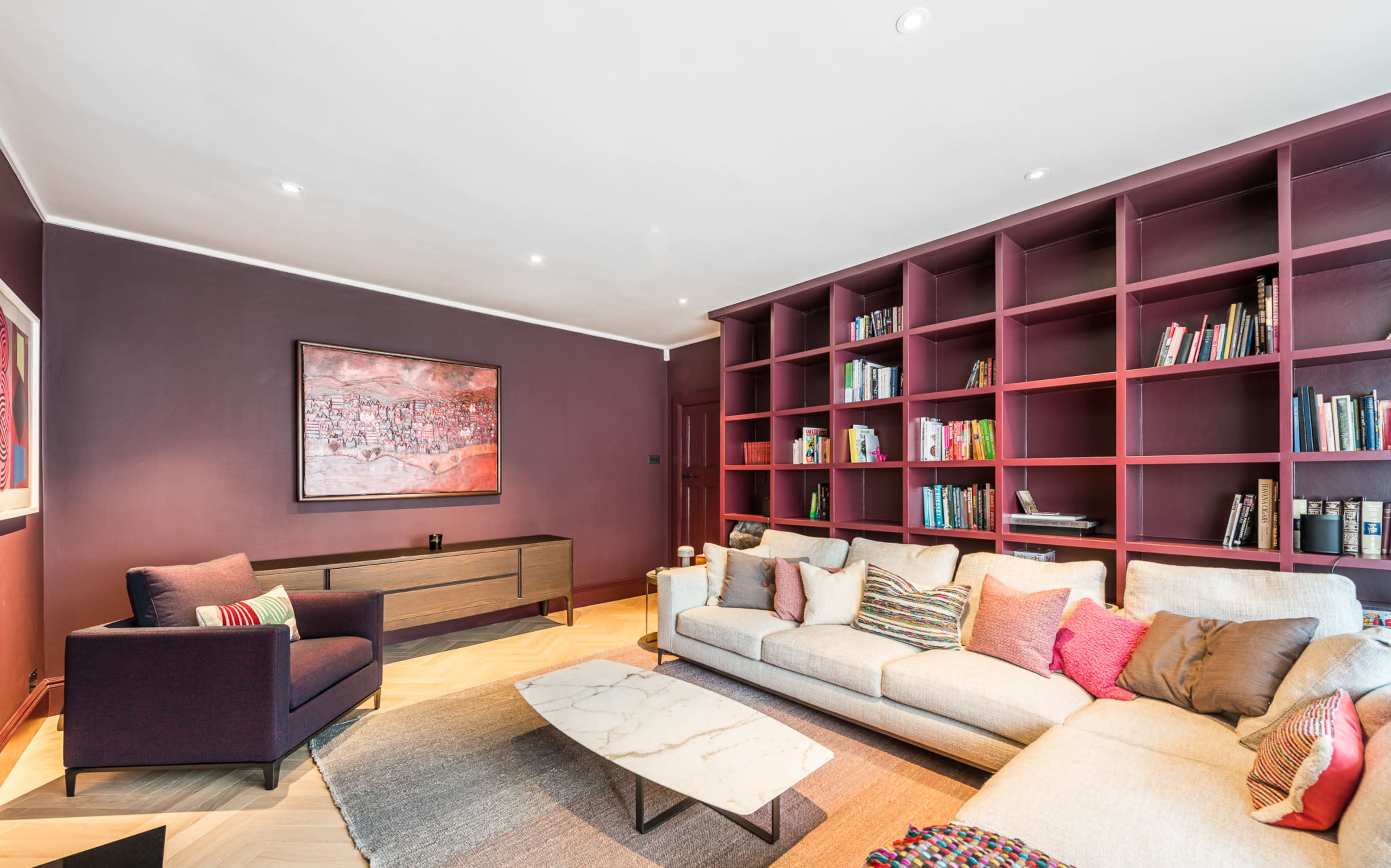 The living room features a sectional sofa and a lounge chair, with a large wall unit filled with books and decorative items, all set against a deep-colored wall.