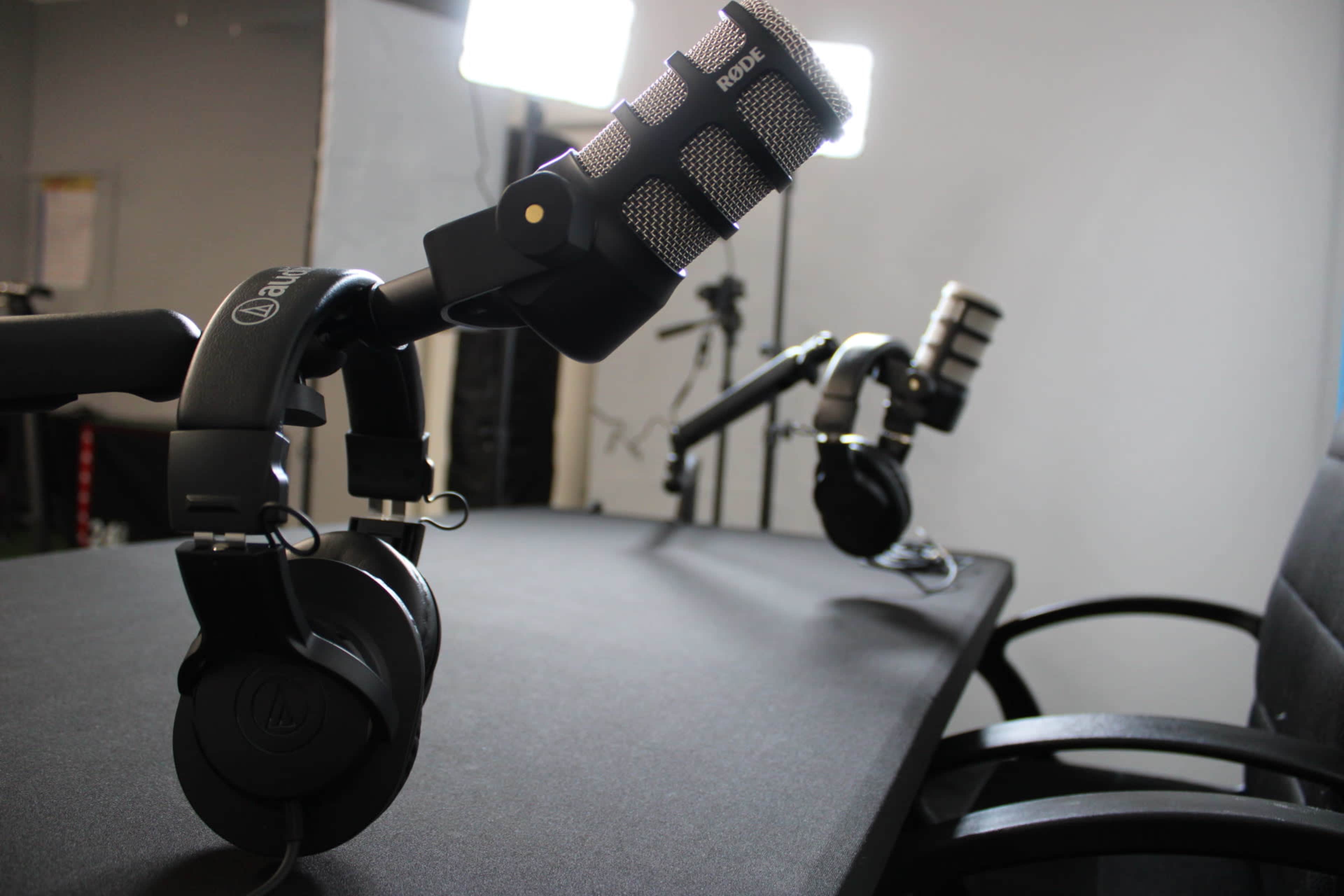 The image shows a recording setup with two microphones mounted on adjustable arms and black headphones placed on a table.