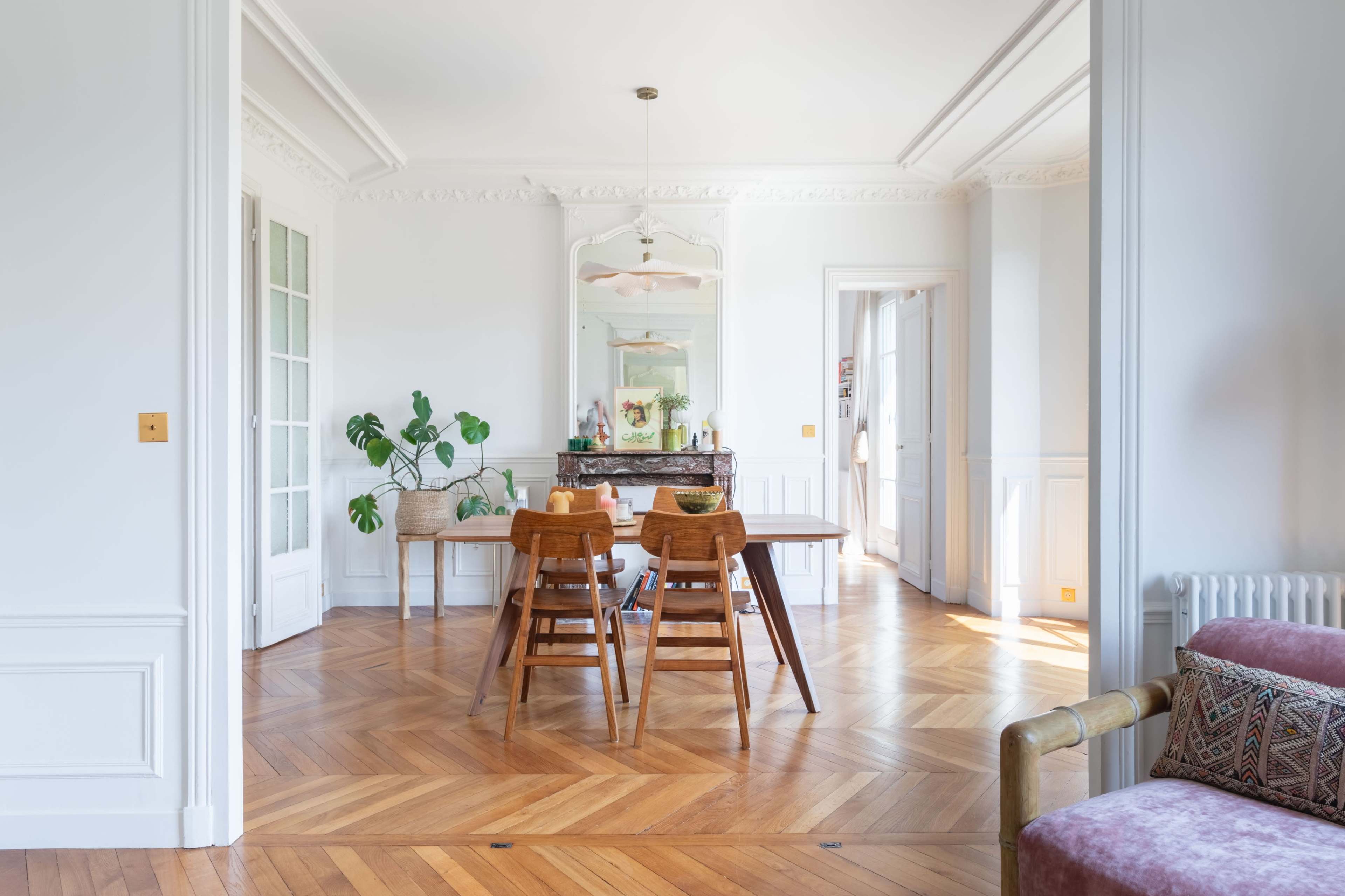 A bright, modern dining area with a wooden table and four chairs, set against a backdrop of light-colored walls and herringbone-patterned flooring.
