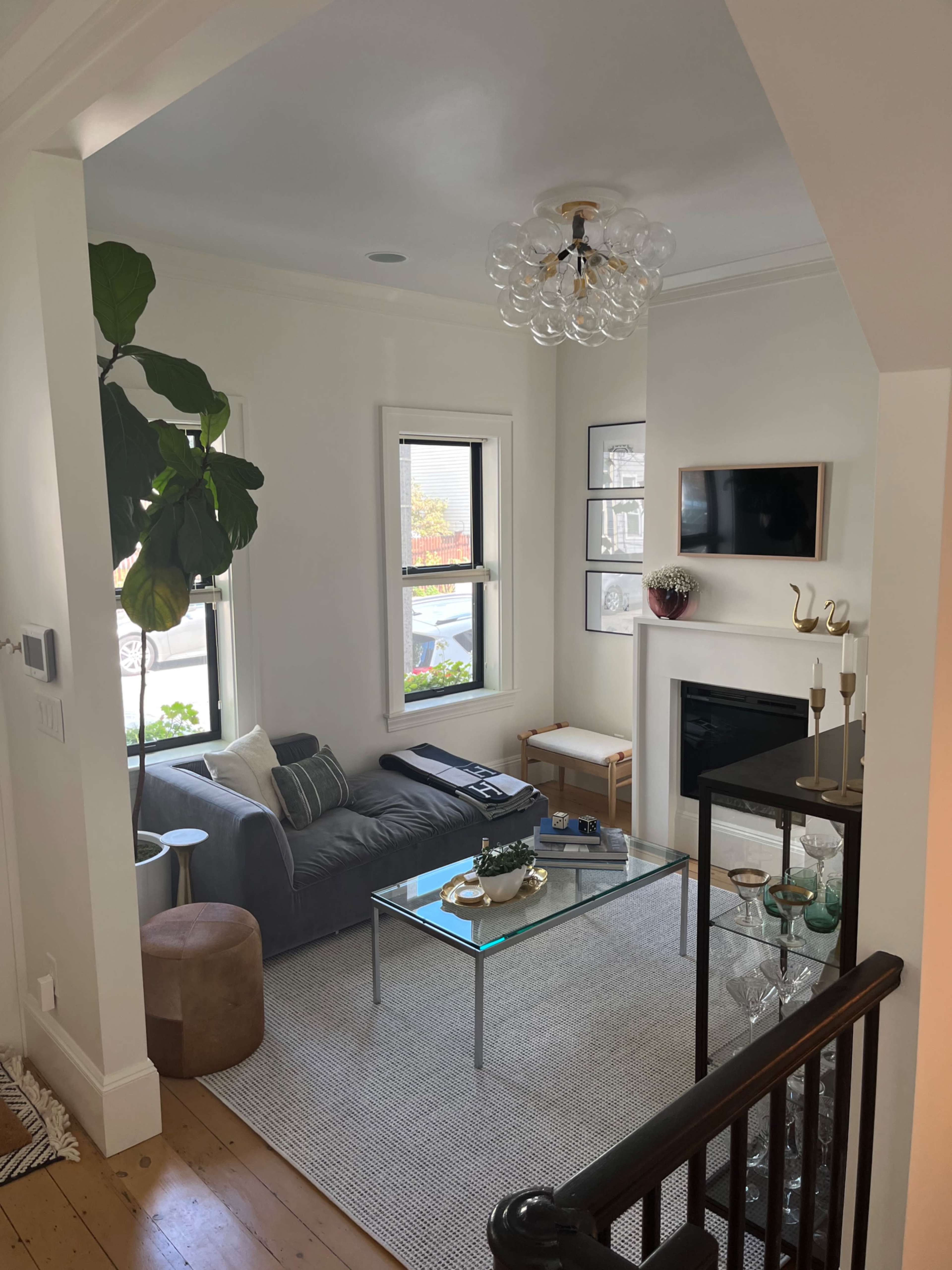 A modern living room with a gray sofa, a glass coffee table, a fireplace, and a plant in the corner.