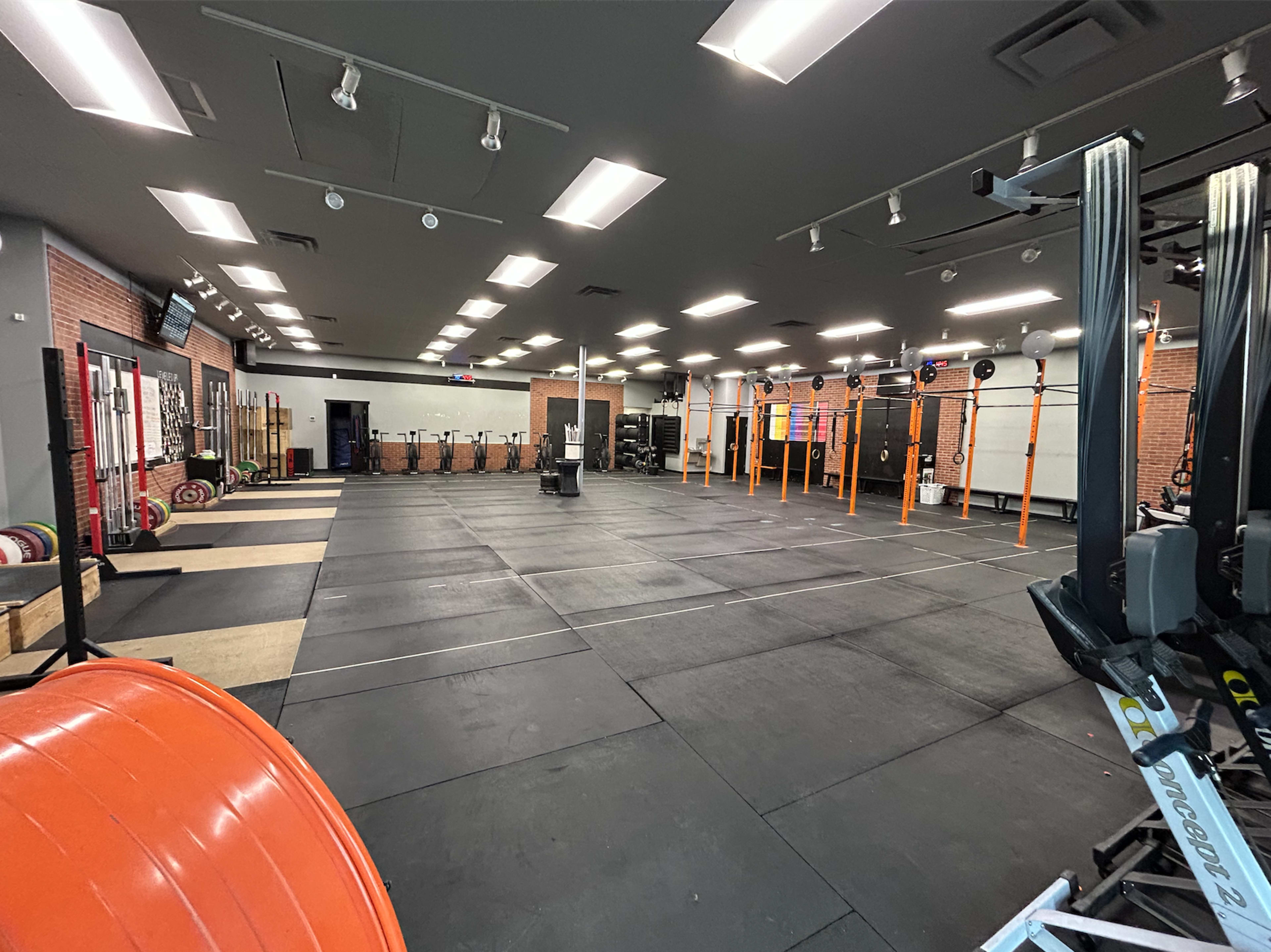 An empty gym space with weightlifting equipment, platforms, and exercise machines arranged on a black rubber floor.
