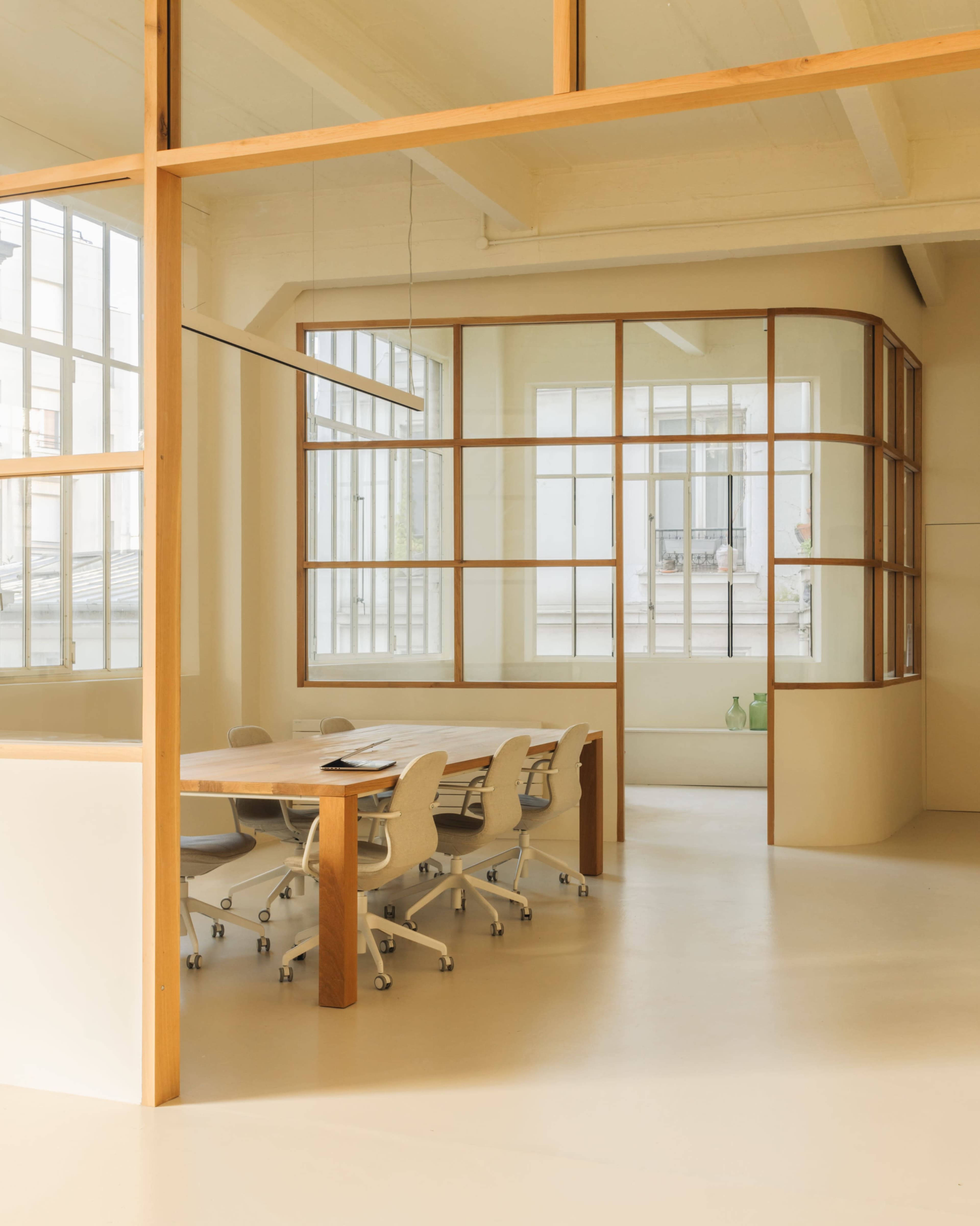 A modern conference room featuring a long wooden table surrounded by ergonomic chairs, with large windows providing natural light.