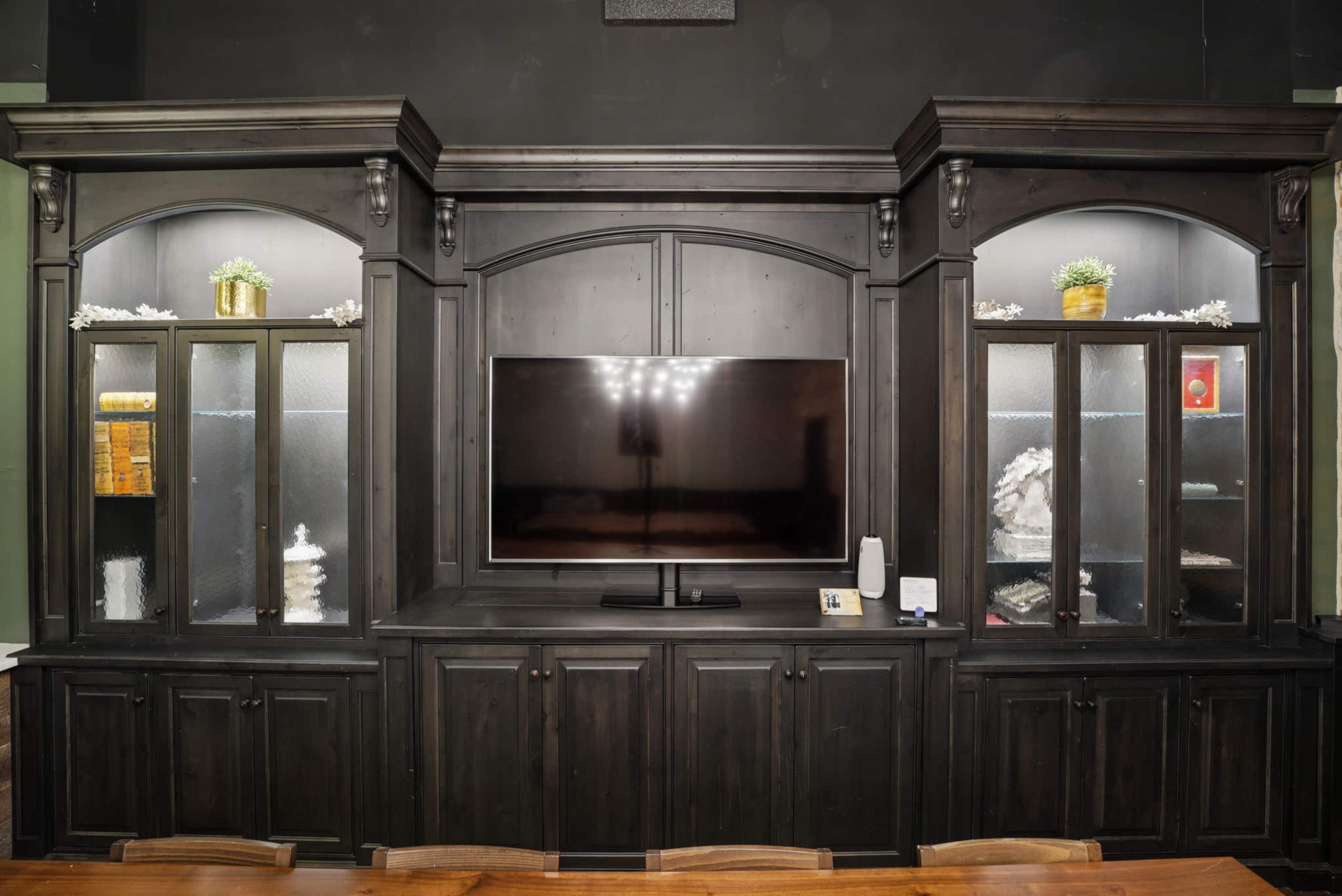 The image shows a large black wooden entertainment unit with glass display cabinets on either side of a flat-screen television.