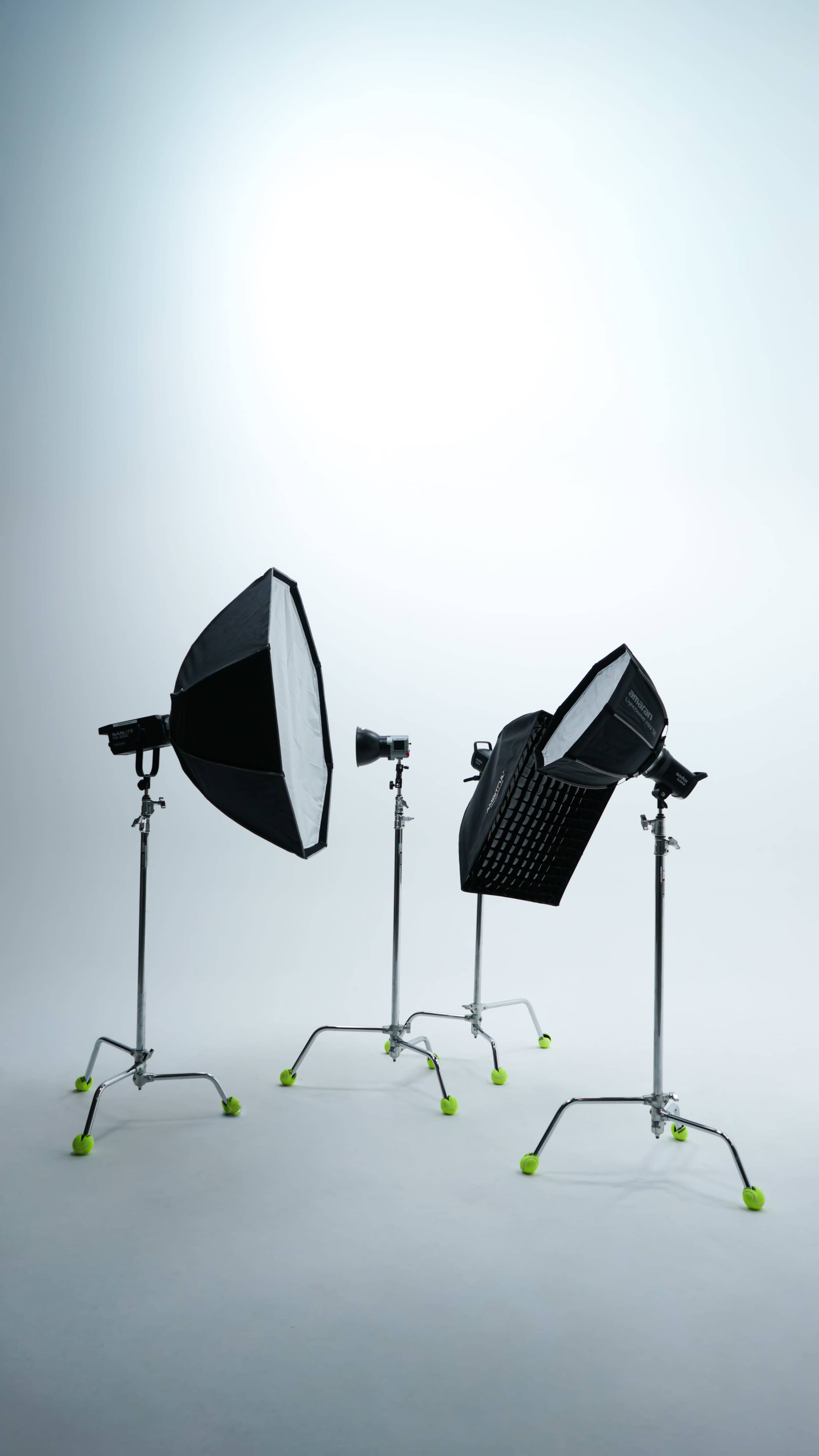 The image shows three studio light setups with umbrellas and softboxes on adjustable stands against a plain background.