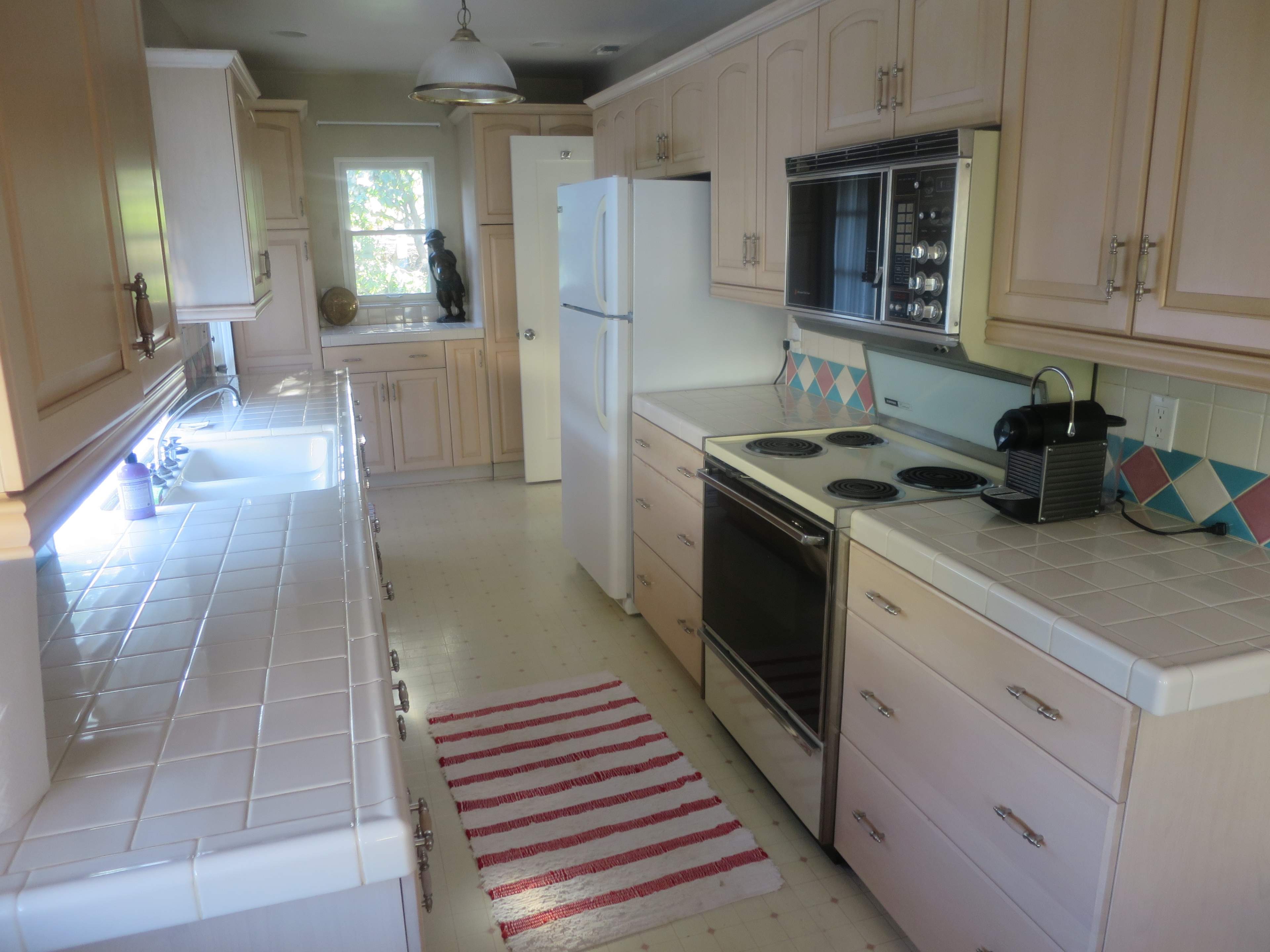 A kitchen with beige cabinetry, white countertops, and various appliances, including a refrigerator and an oven, arranged along the walls.