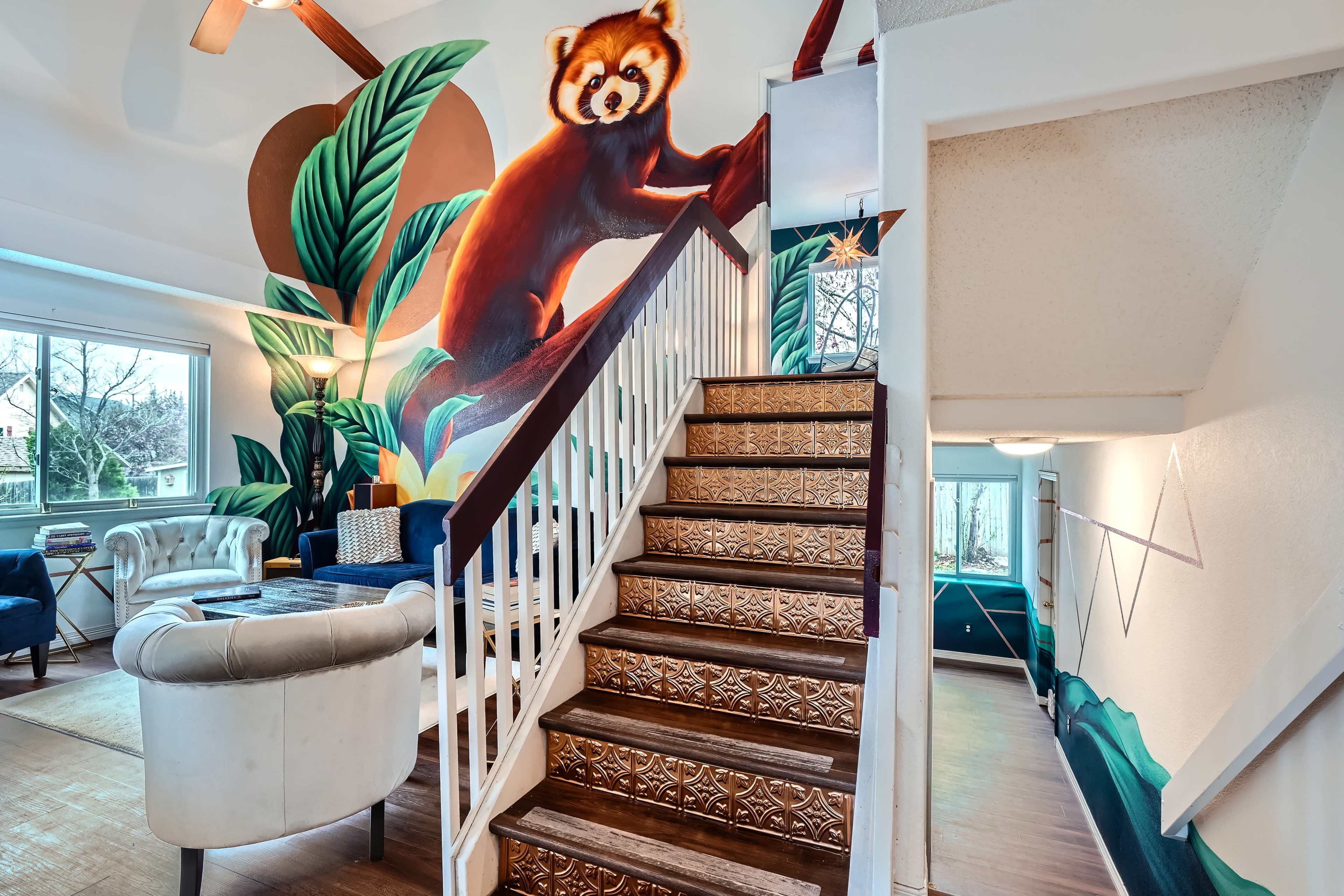 A staircase with decorative wooden steps leads up from a room featuring large botanical murals and a sitting area.