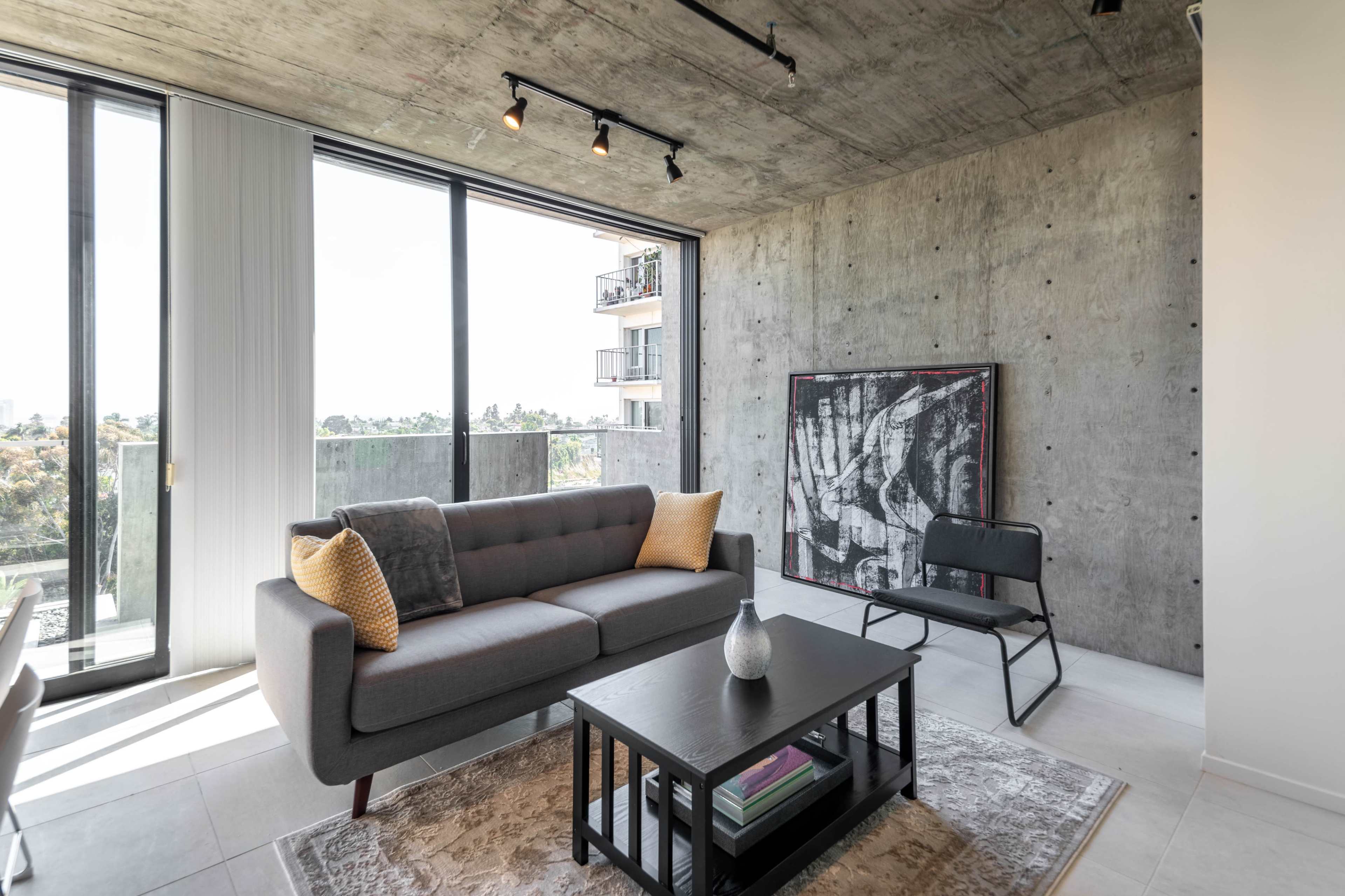 A modern living room with a gray couch, a black coffee table, and a large window displaying an outdoor view.