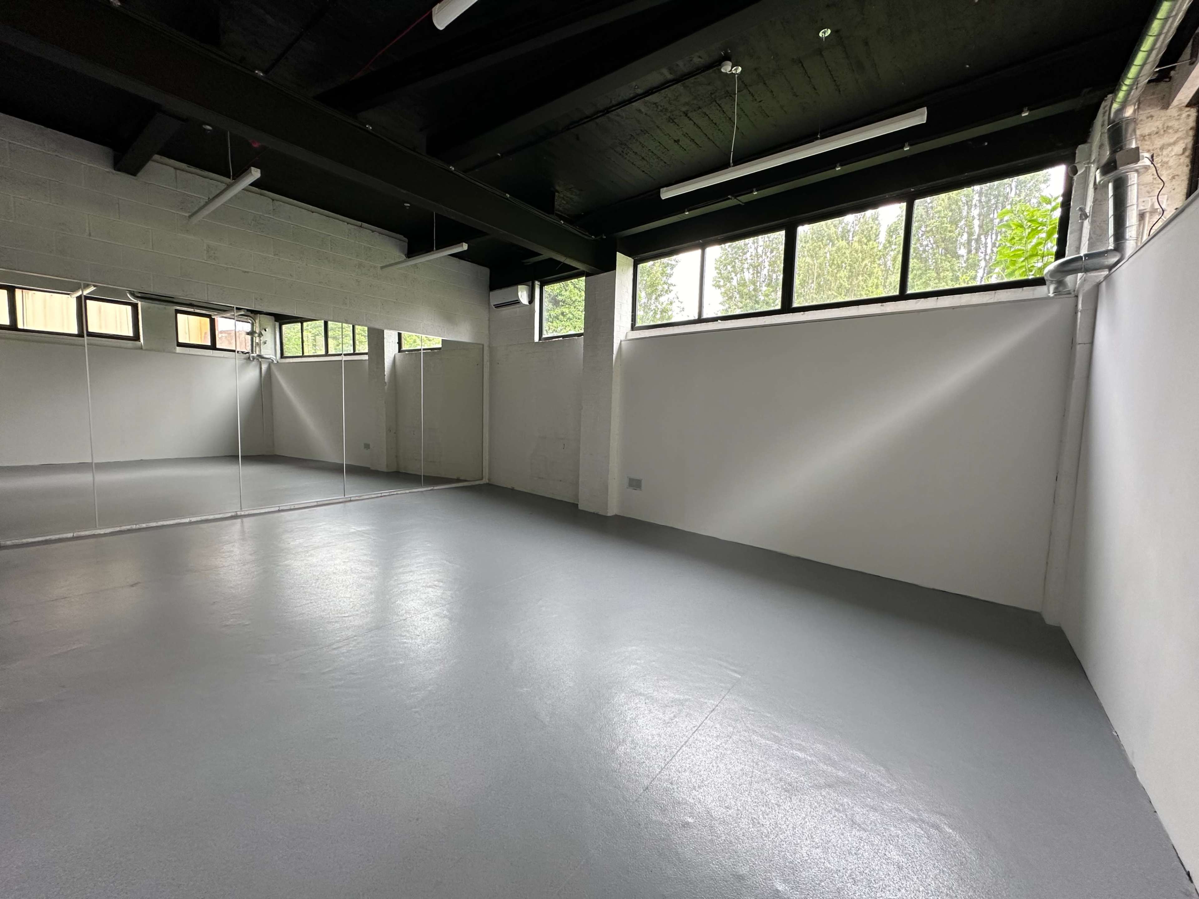 The image shows an empty room with a gray floor, large windows, and a mirrored wall reflecting the interior.