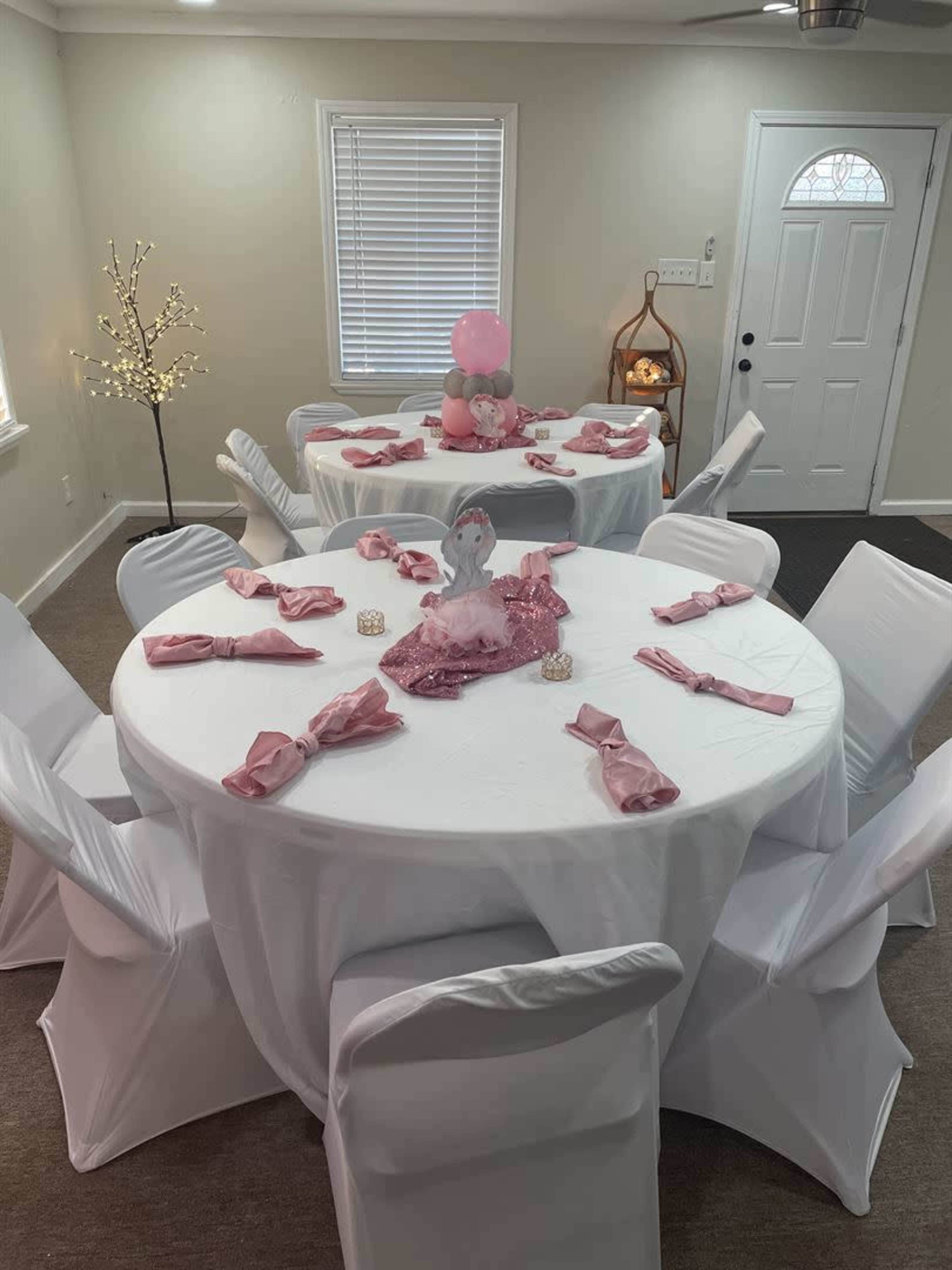 A banquet area with multiple round tables covered in white tablecloths, each set with pink napkins and a decorative centerpiece.