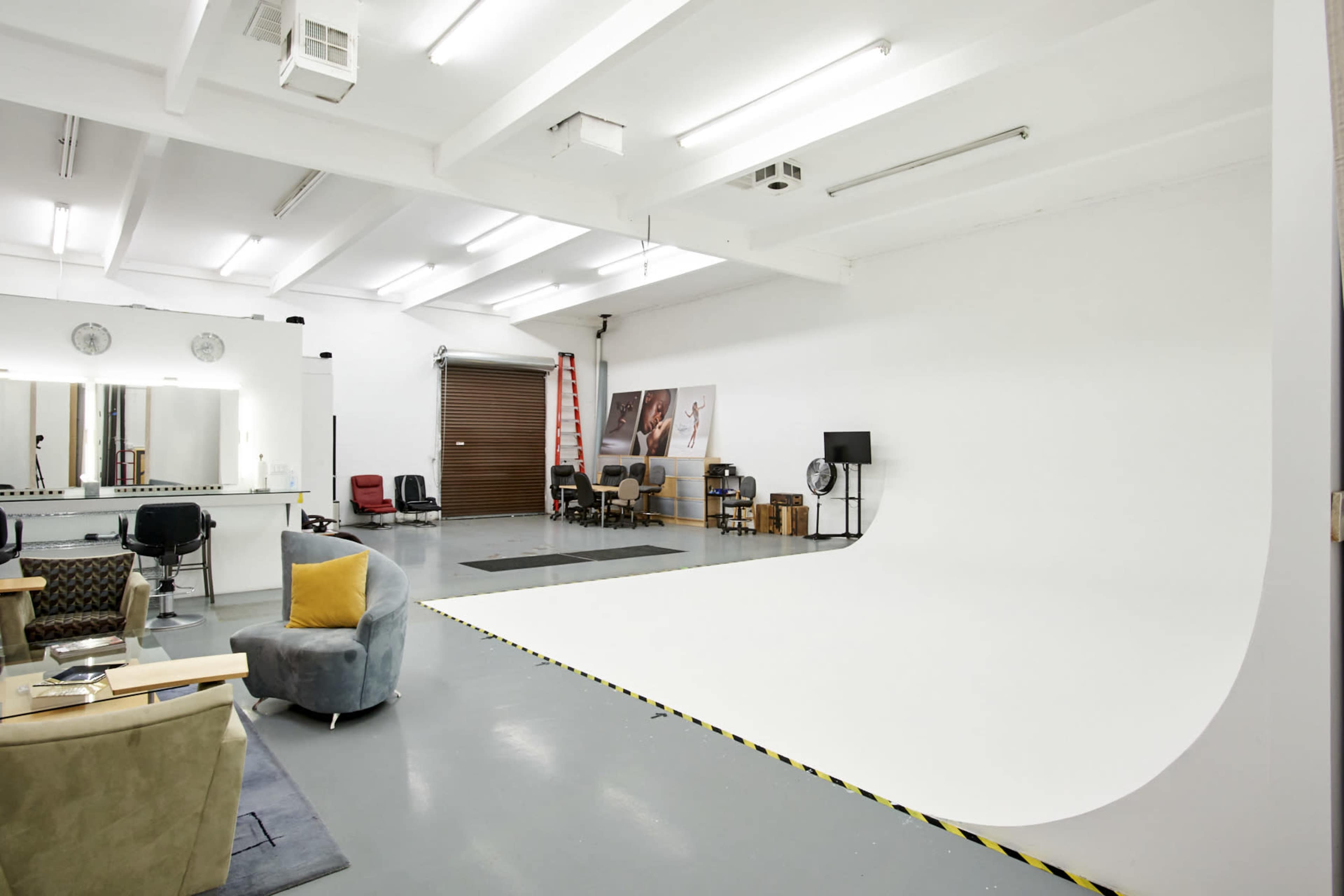 A spacious, well-lit photo studio with a large seamless backdrop, mirrored workstation, and seating areas.