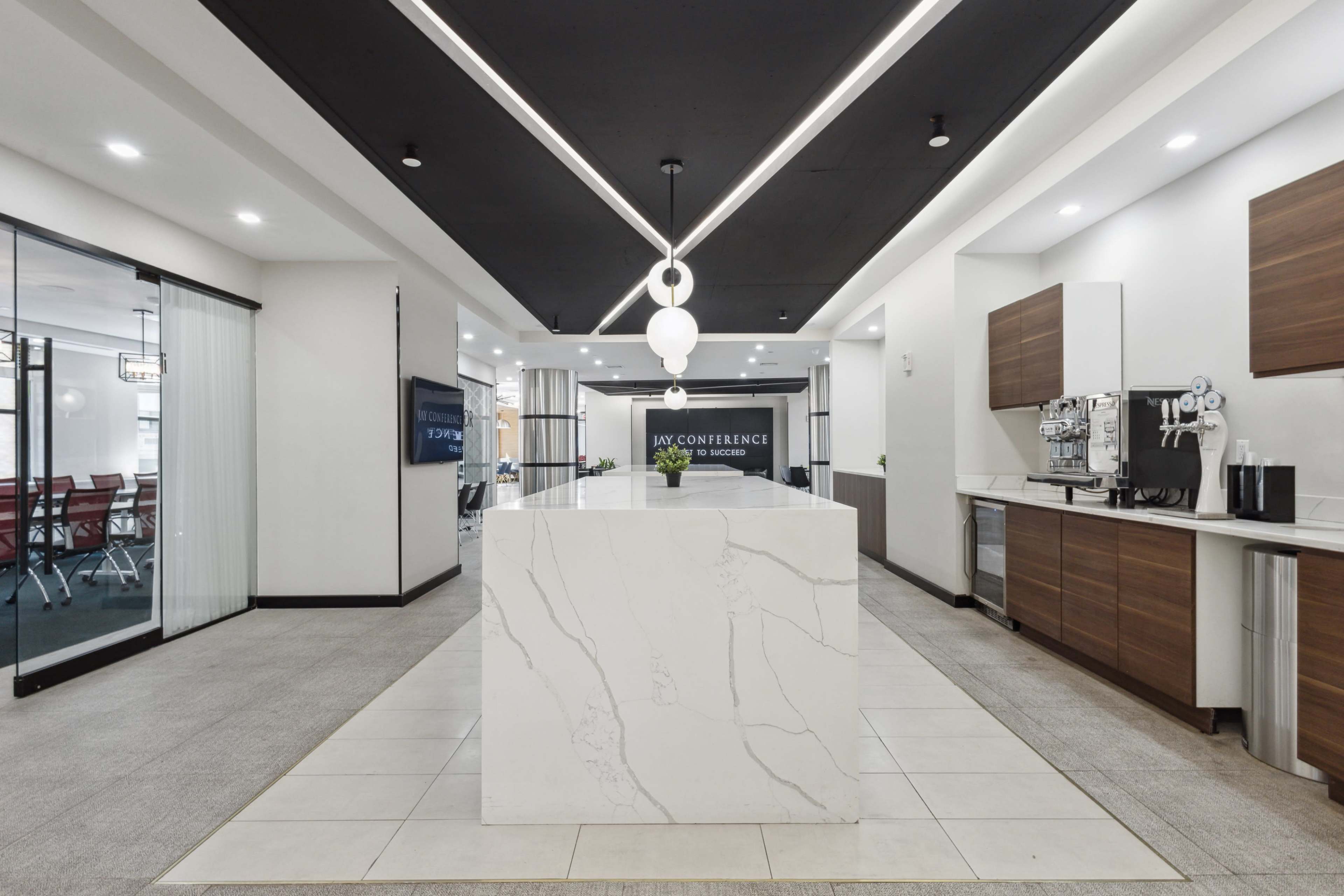 A modern conference center lobby with a marble reception desk, wooden cabinetry, and a coffee station along one side.